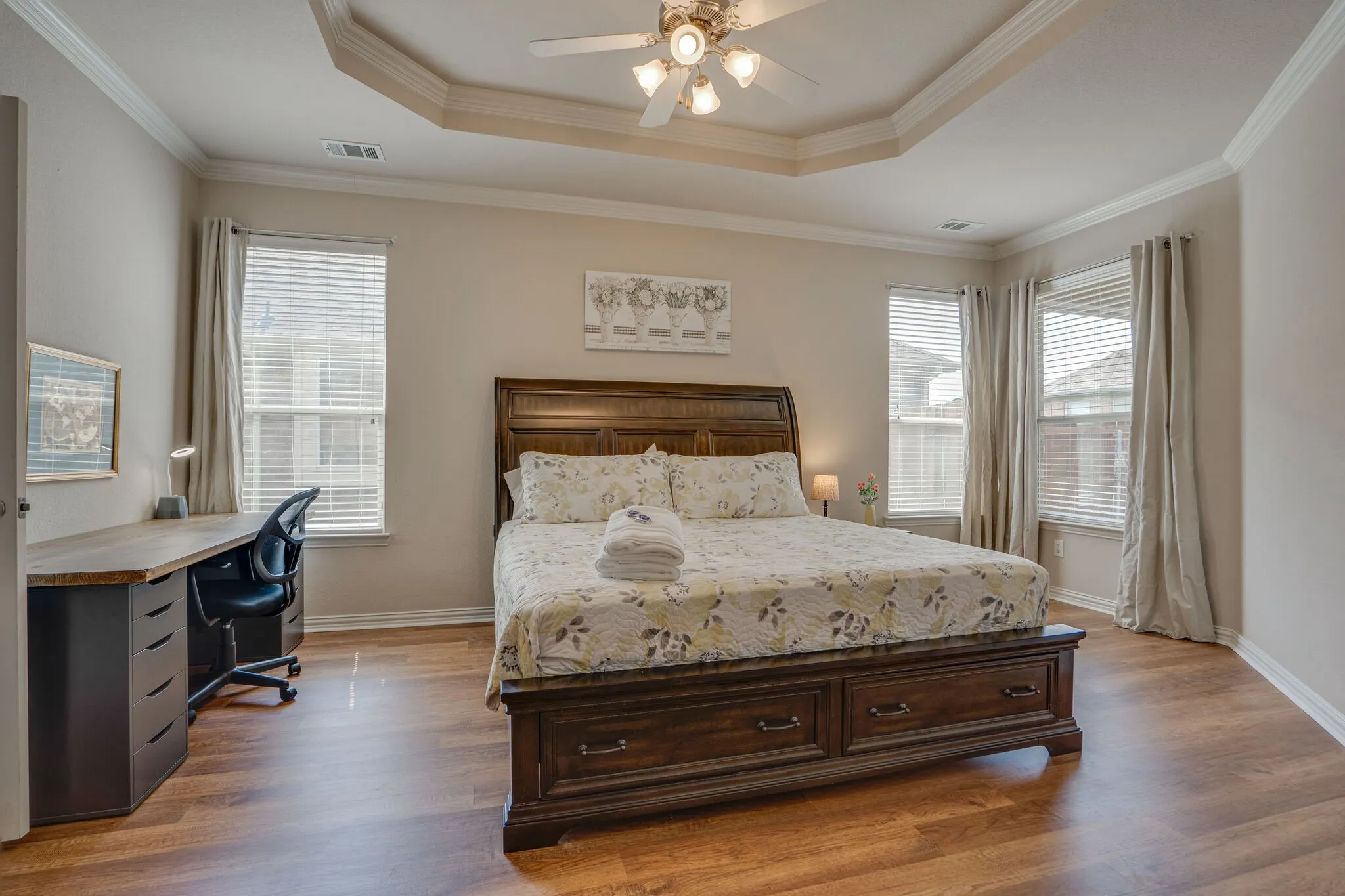 Tray ceiling with crown molding, wood-finish flooring, multiple windows with blinds, and a ceiling fan with integrated lighting