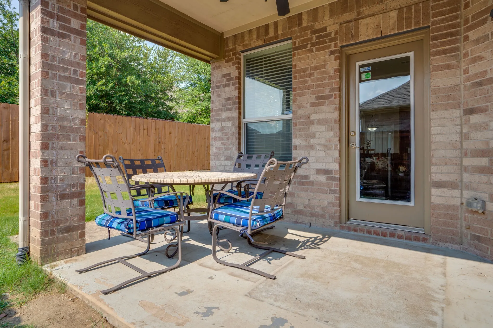 Covered patio featuring brick columns, a full-lite exterior door, and a privacy fence