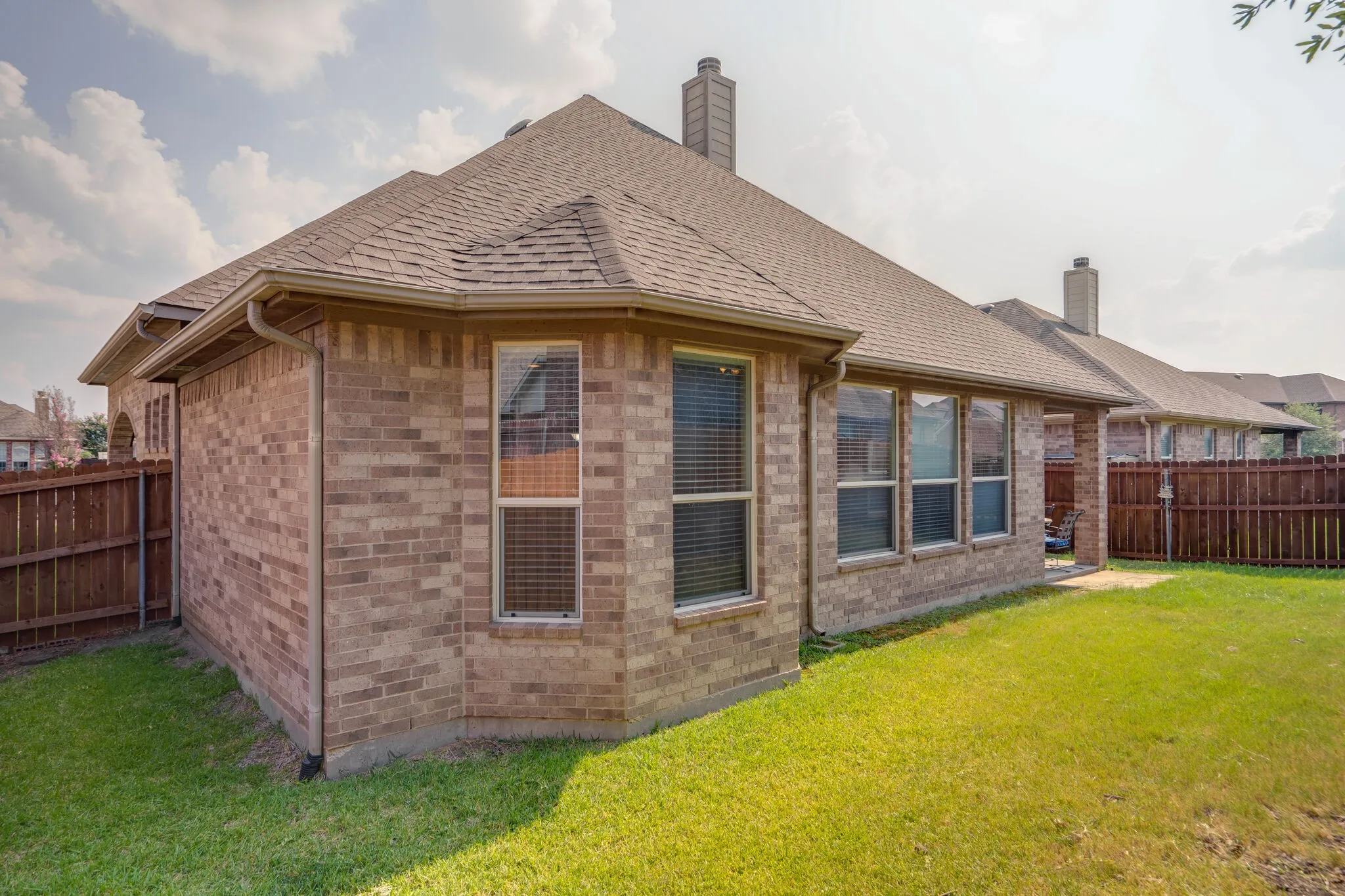 Brick exterior, gabled roofline, multiple windows, brown privacy fencing, and chimneys