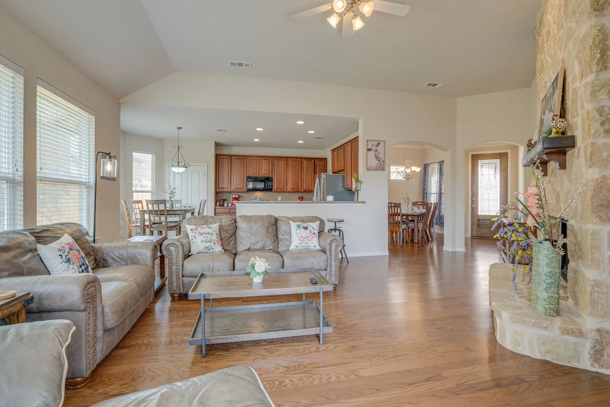 Vaulted ceilings, wood-finish flooring, stone fireplace, recessed lighting, and a ceiling fan
