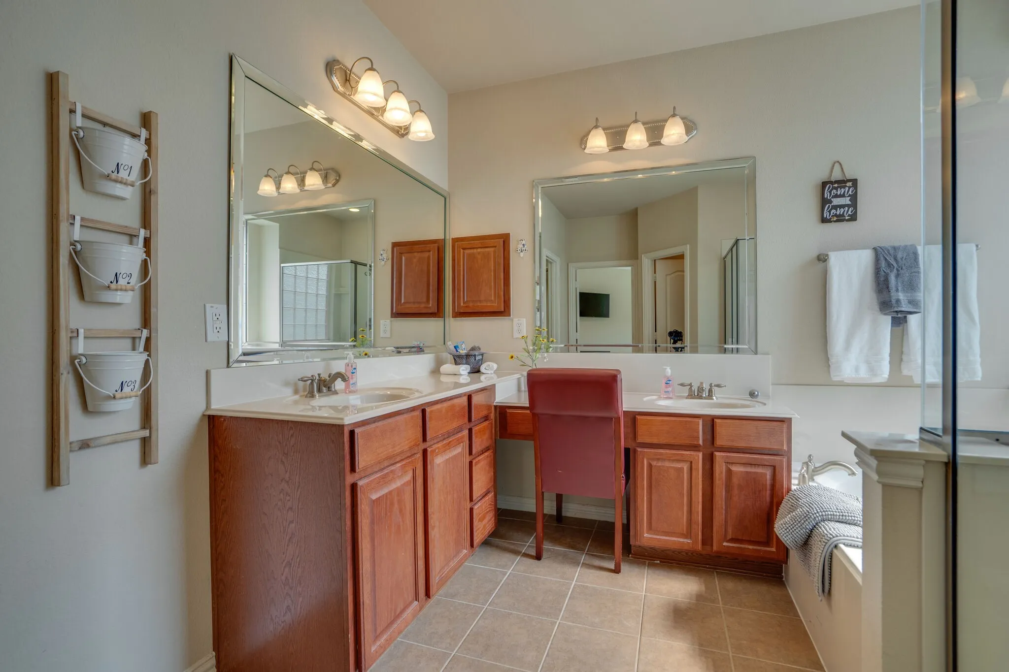 Dual vanities with integrated sinks, wood-finish cabinetry, and expansive wall-mounted mirrors
