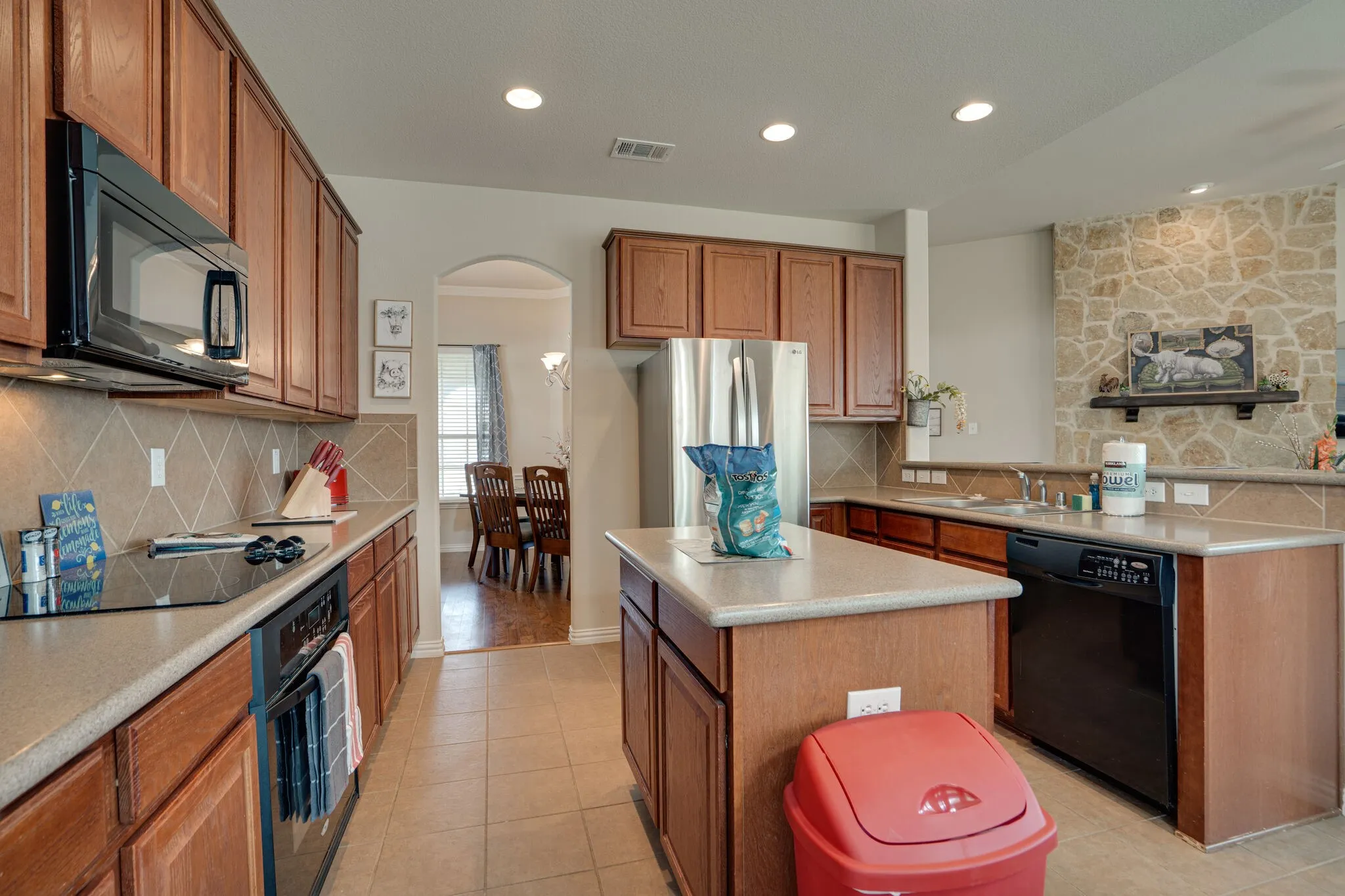 Kitchen featuring wood cabinetry, stone-look countertops, stainless steel appliances, and a tiled backsplash
