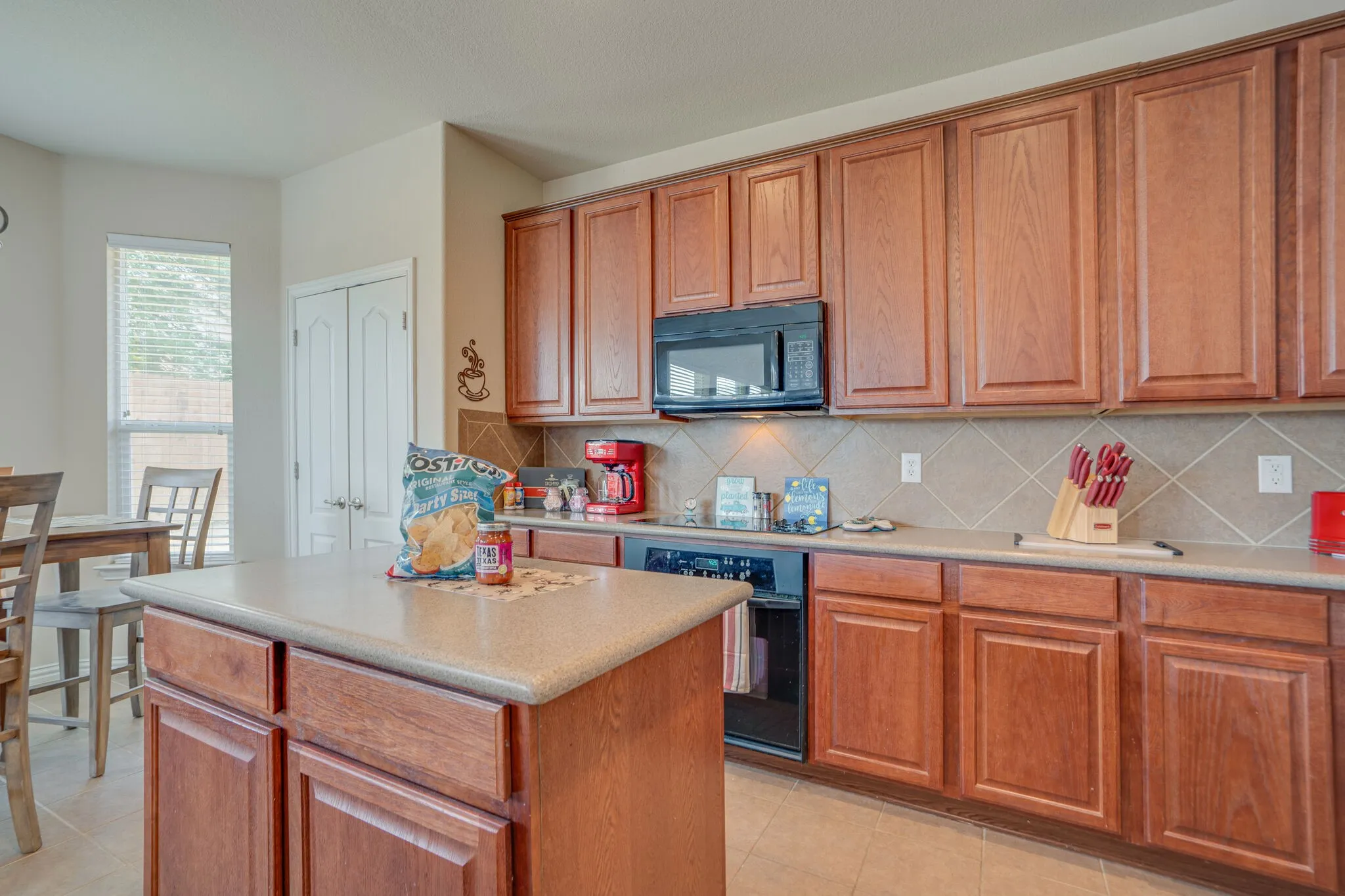 Kitchen featuring wood-finish cabinetry, a central island, integrated black microwave, tiled backsplash, and light countertops