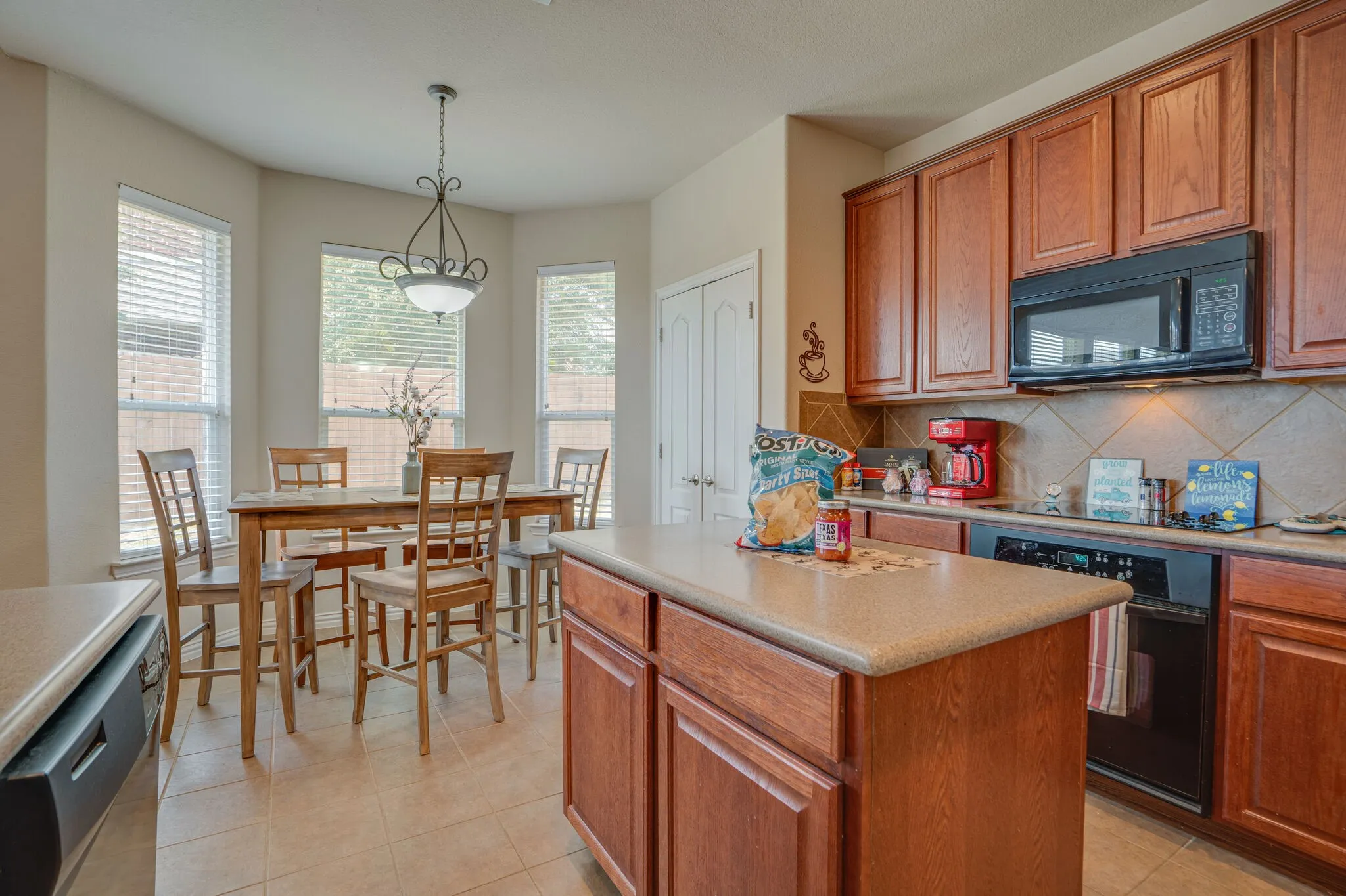 Wood-finish cabinetry with black appliances, tile backsplash, and a central island with countertop