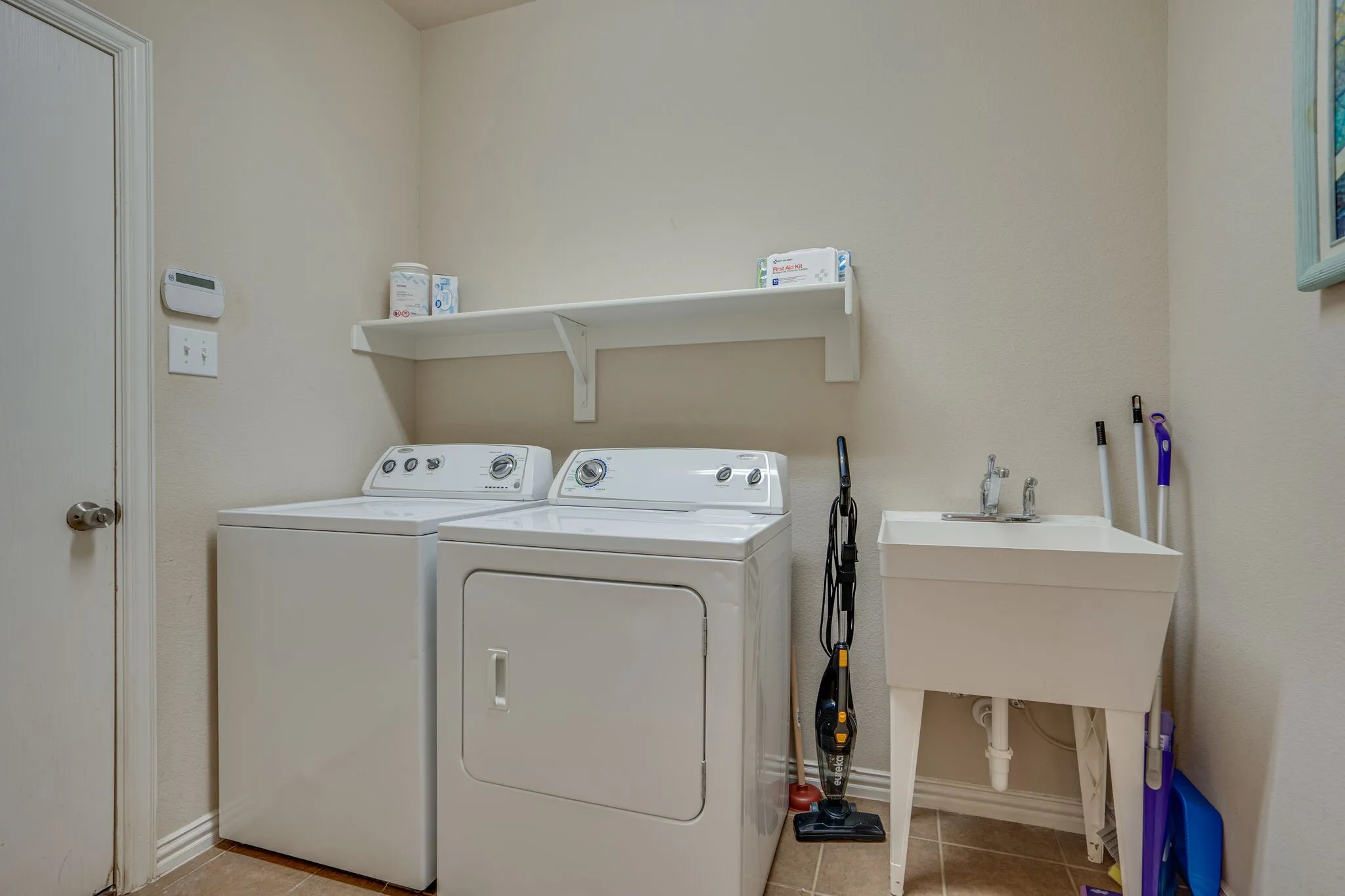 Utility room featuring a built-in shelf, a utility sink with a chrome faucet, and tiled flooring