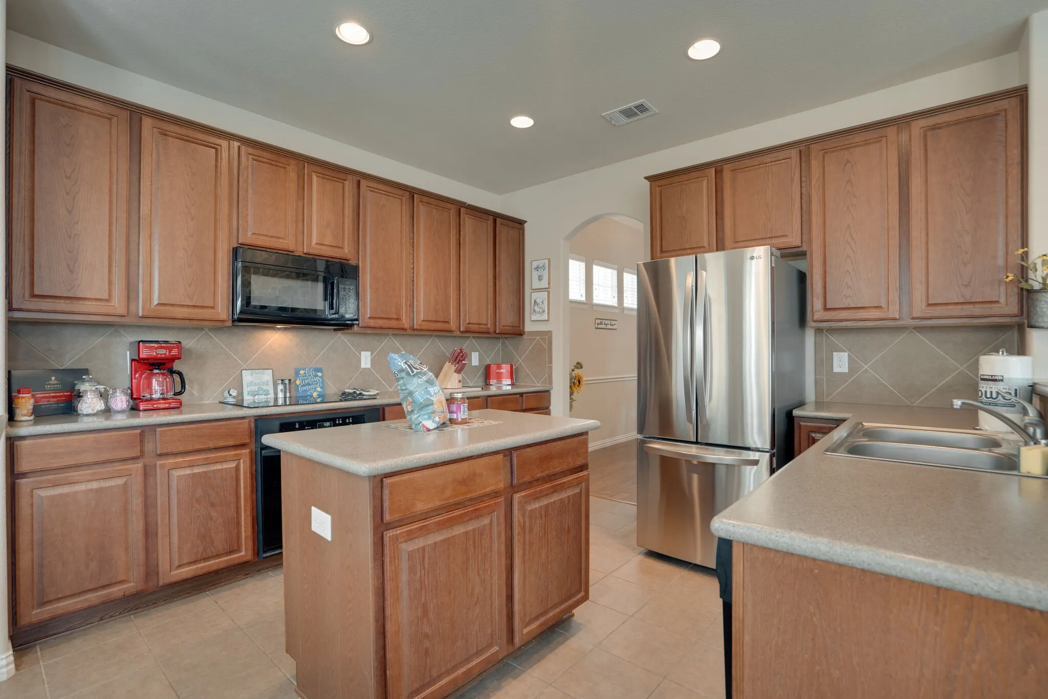 Kitchen featuring a central island, wood-finish cabinetry, stainless steel appliances, a double basin sink, and a tiled backsplash