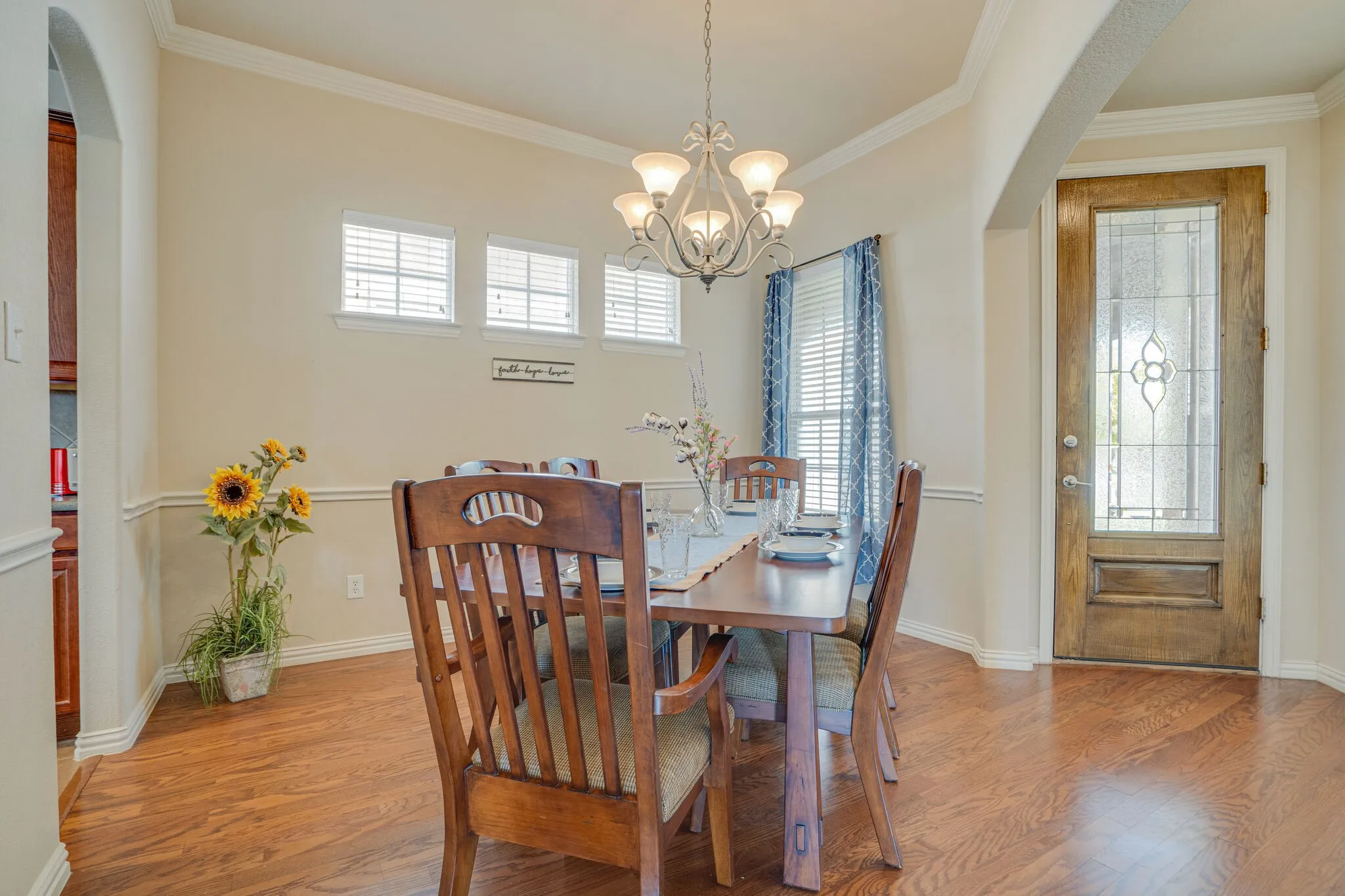 Wood-finish flooring, decorative chandelier, three transom windows, a wood-paneled door with leaded glass, and crown molding