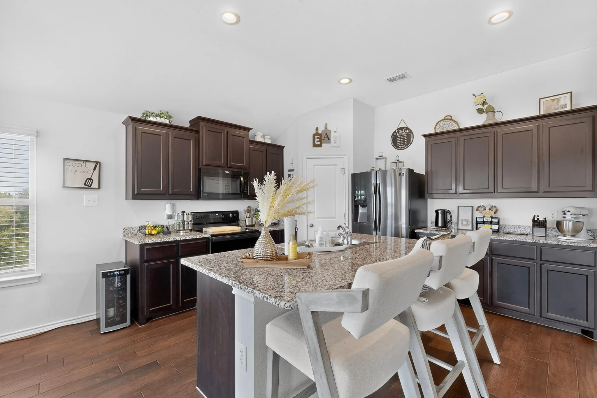 Kitchen featuring dark wood cabinetry, granite countertops, wood-finish flooring, a stainless steel refrigerator, and recessed lighting