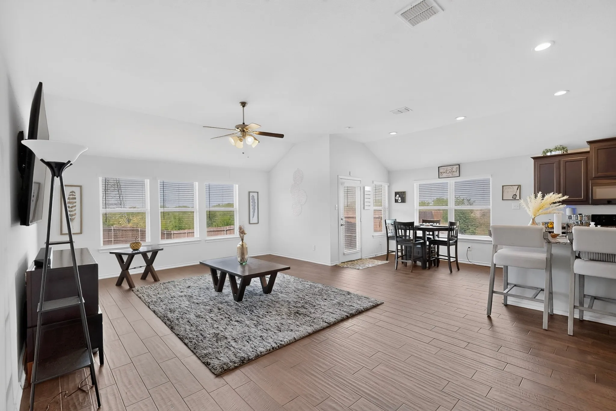 Vaulted ceilings with a ceiling fan, wood-finish flooring, a kitchen island with seating, a dining area, and multiple windows