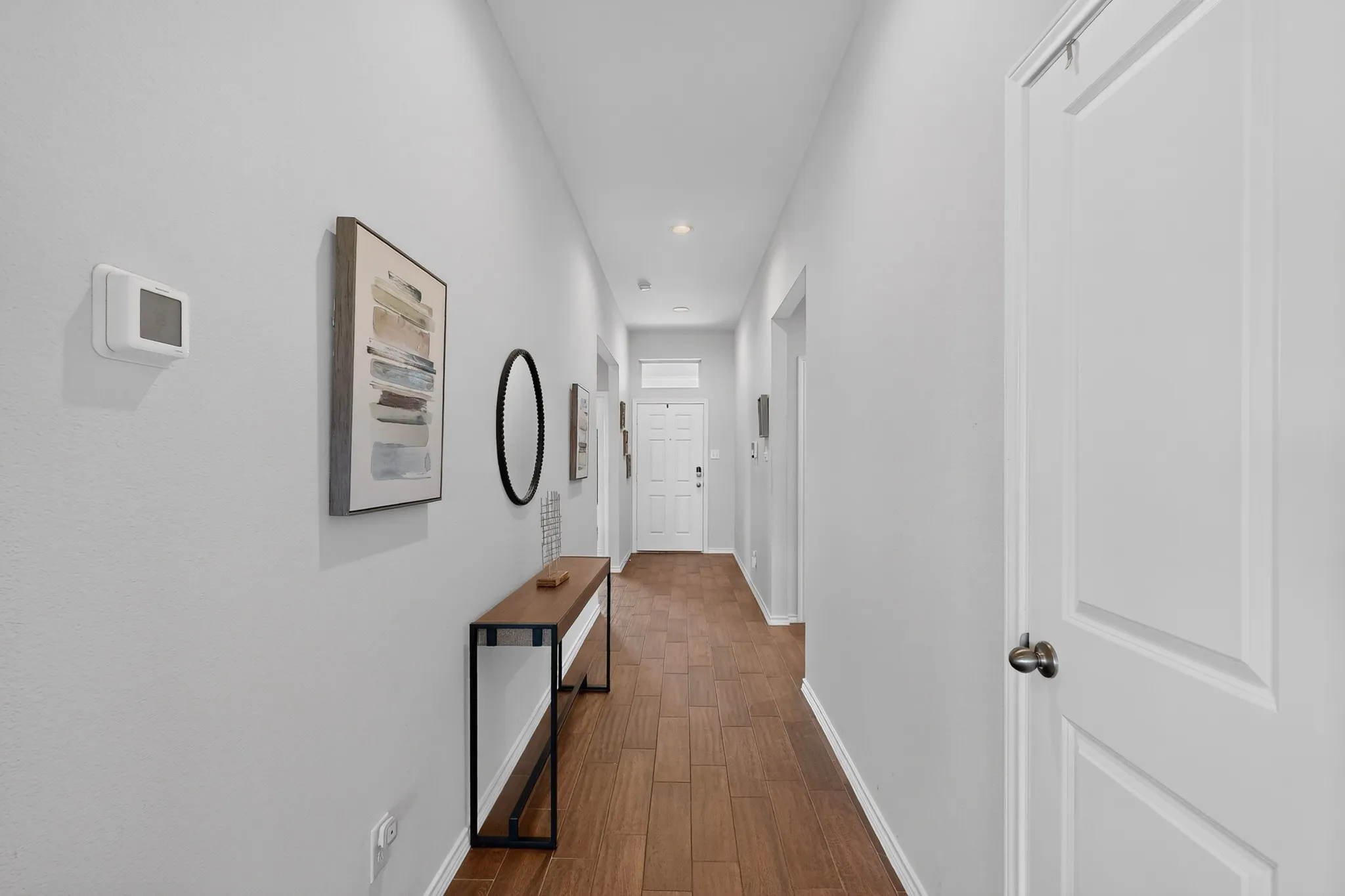 Wood-finish flooring throughout a neutral-toned hallway with recessed lighting and white paneled doors