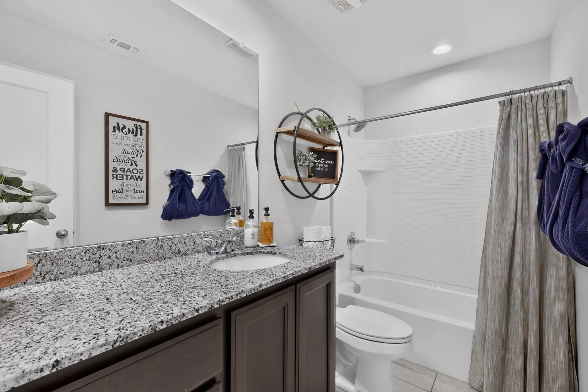 Granite-style countertop with integrated sink, dark wood-finish vanity with cabinet storage, and a white tiled shower/tub combination