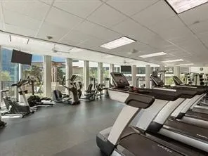 Fitness center with expansive window walls, ceiling-mounted televisions, and recessed lighting