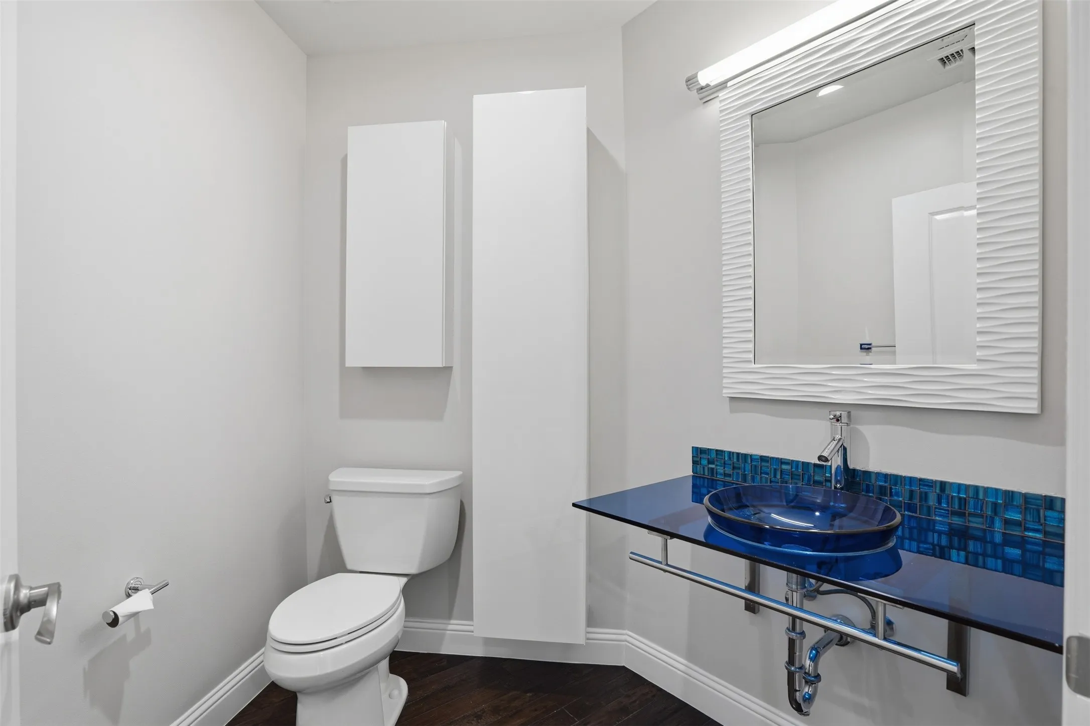 Powder room featuring a blue glass vessel sink, floating glass countertop, mosaic tile backsplash, and two wall-mounted storage cabinets