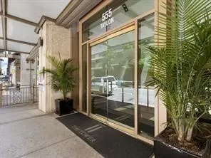 Building entrance featuring glass doors, a prominent address display, an overhead canopy, and decorative potted plants