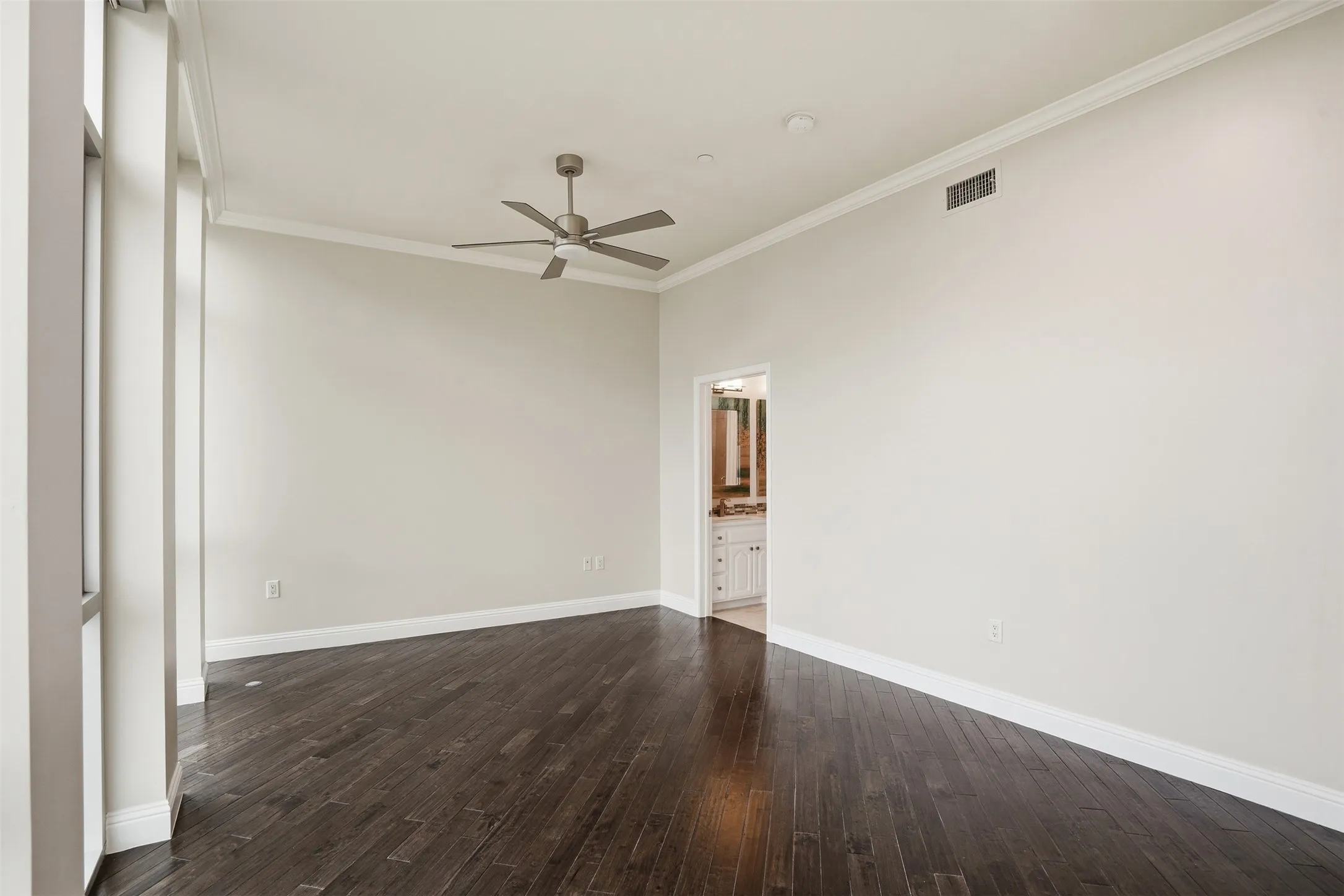 Expansive interior featuring dark wood-finish flooring, tall windows, a ceiling fan, and crown molding