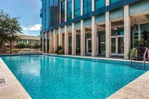 Outdoor swimming pool with concrete decking, glass-front building, and columned architectural elements