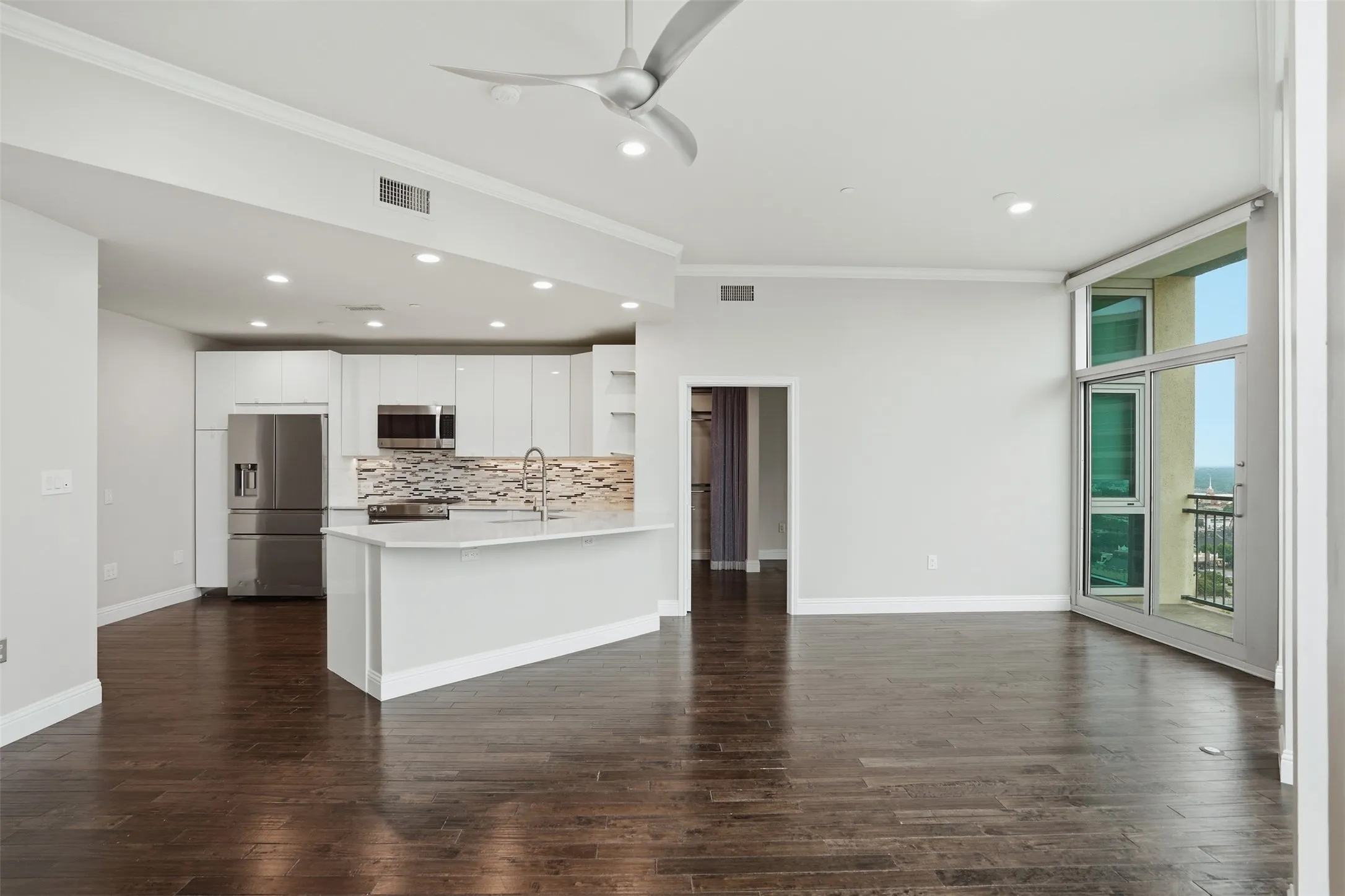 Hardwood flooring throughout, a kitchen featuring an island with a sink, white cabinetry, stainless steel appliances, and a tiled backsplash