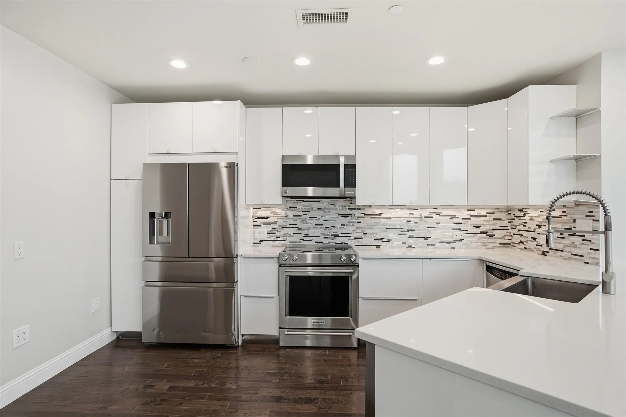 Modern kitchen featuring white flat-panel cabinetry, stainless steel appliances, a mosaic tile backsplash, and wood-finish flooring
