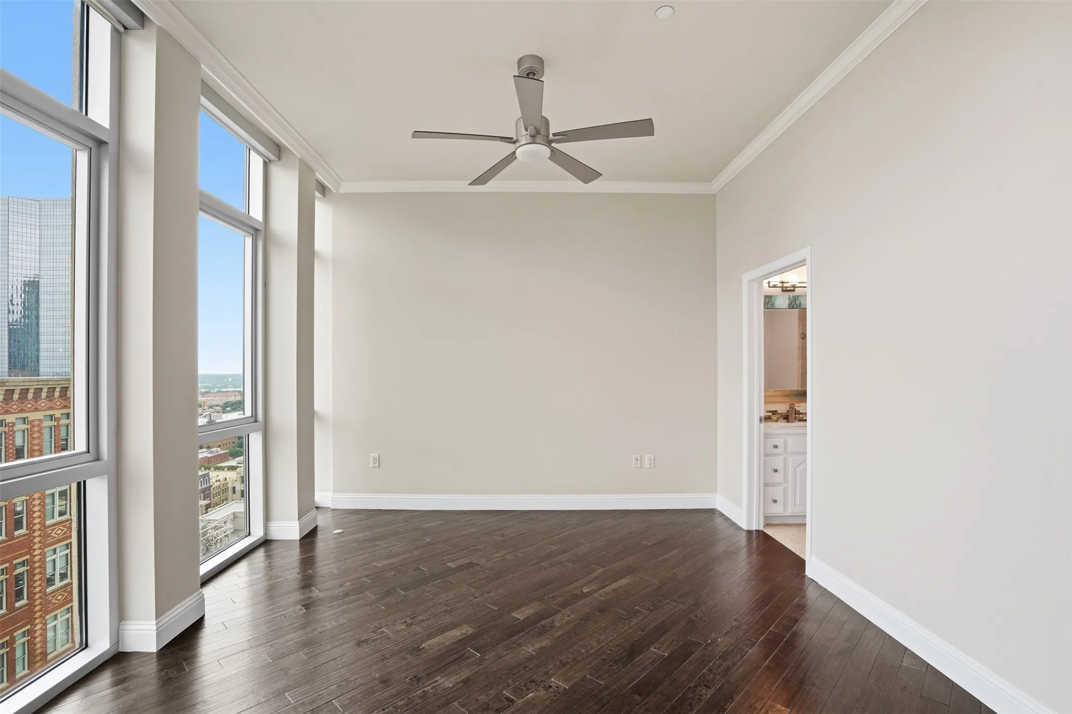 Dark wood-finish flooring, full-height windows, a ceiling fan, and crown molding