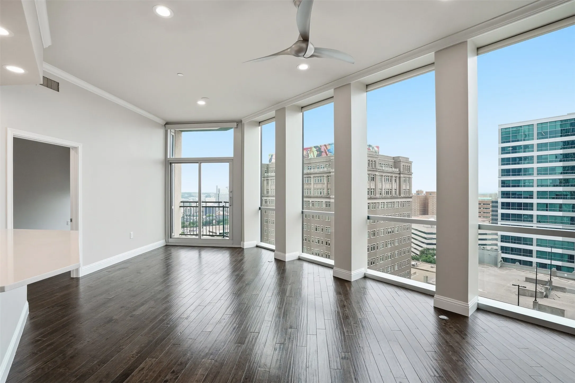 Expansive floor-to-ceiling windows, dark wood-finish flooring, recessed lighting, crown molding, and a modern ceiling fan