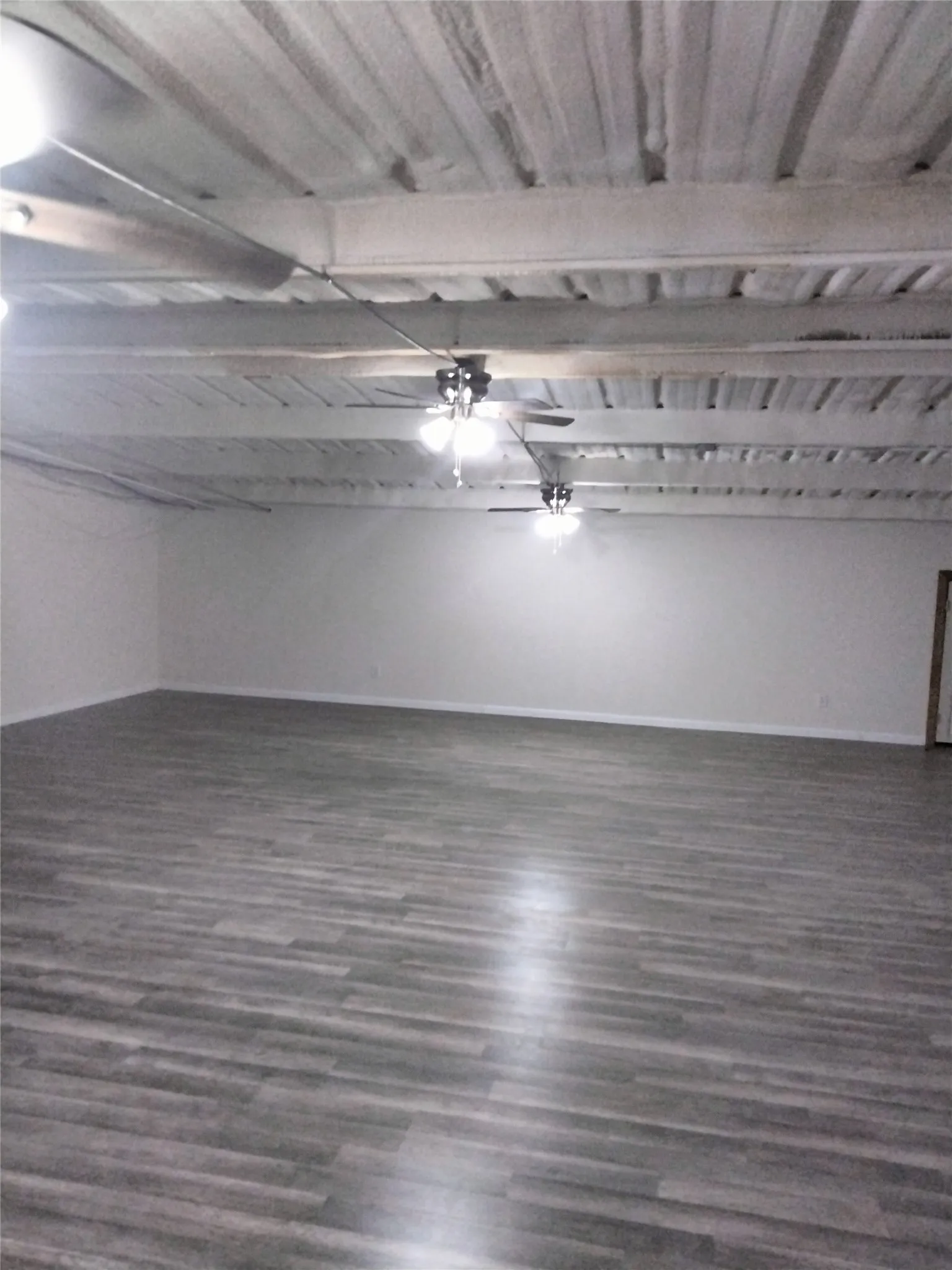 Expansive open-concept room featuring wood-finish flooring, white walls, exposed beam ceiling, and multiple ceiling fans with light fixtures