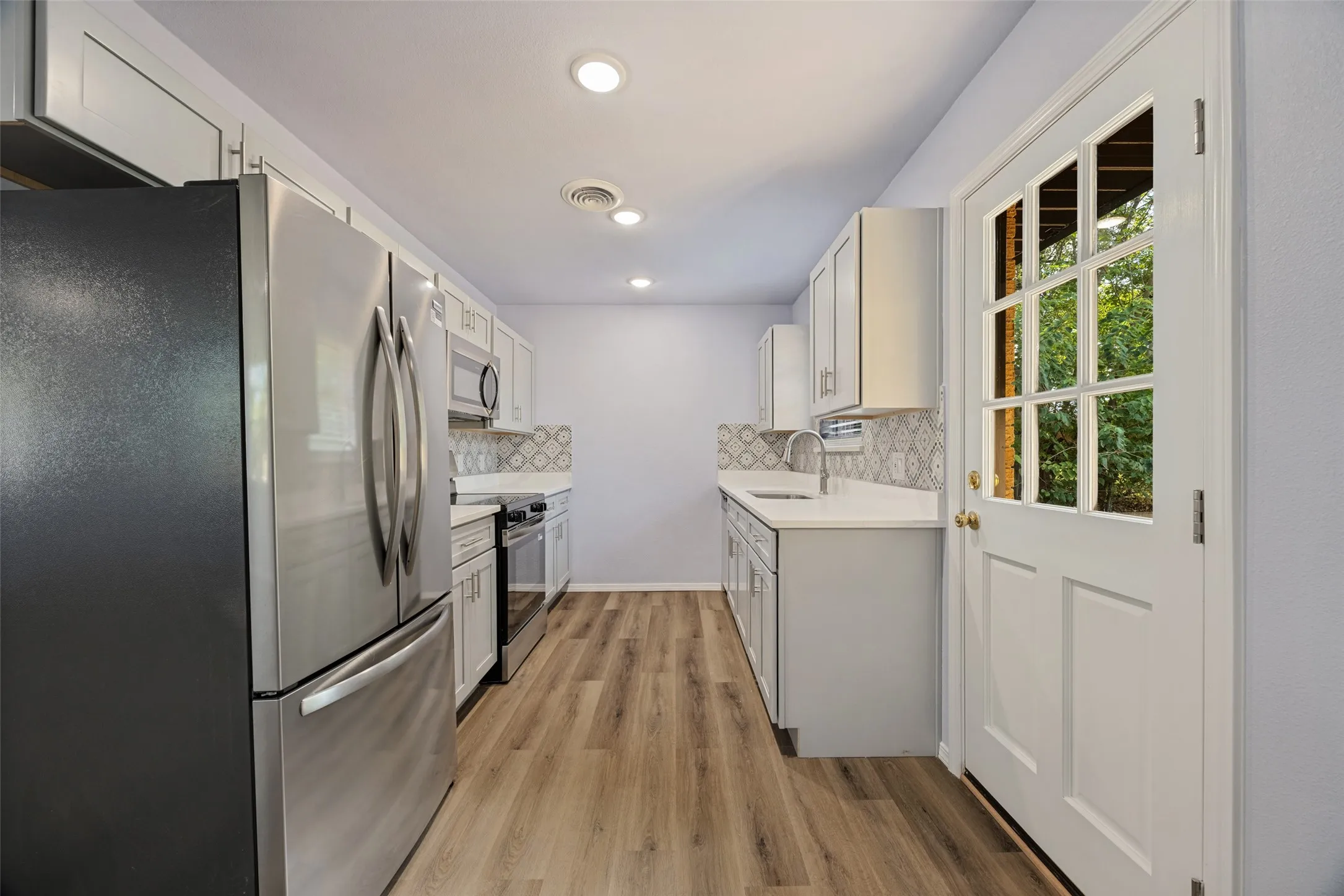 Galley kitchen featuring stainless steel appliances, white cabinetry, wood-finish flooring, recessed lighting, and a white paneled door with glass inserts
