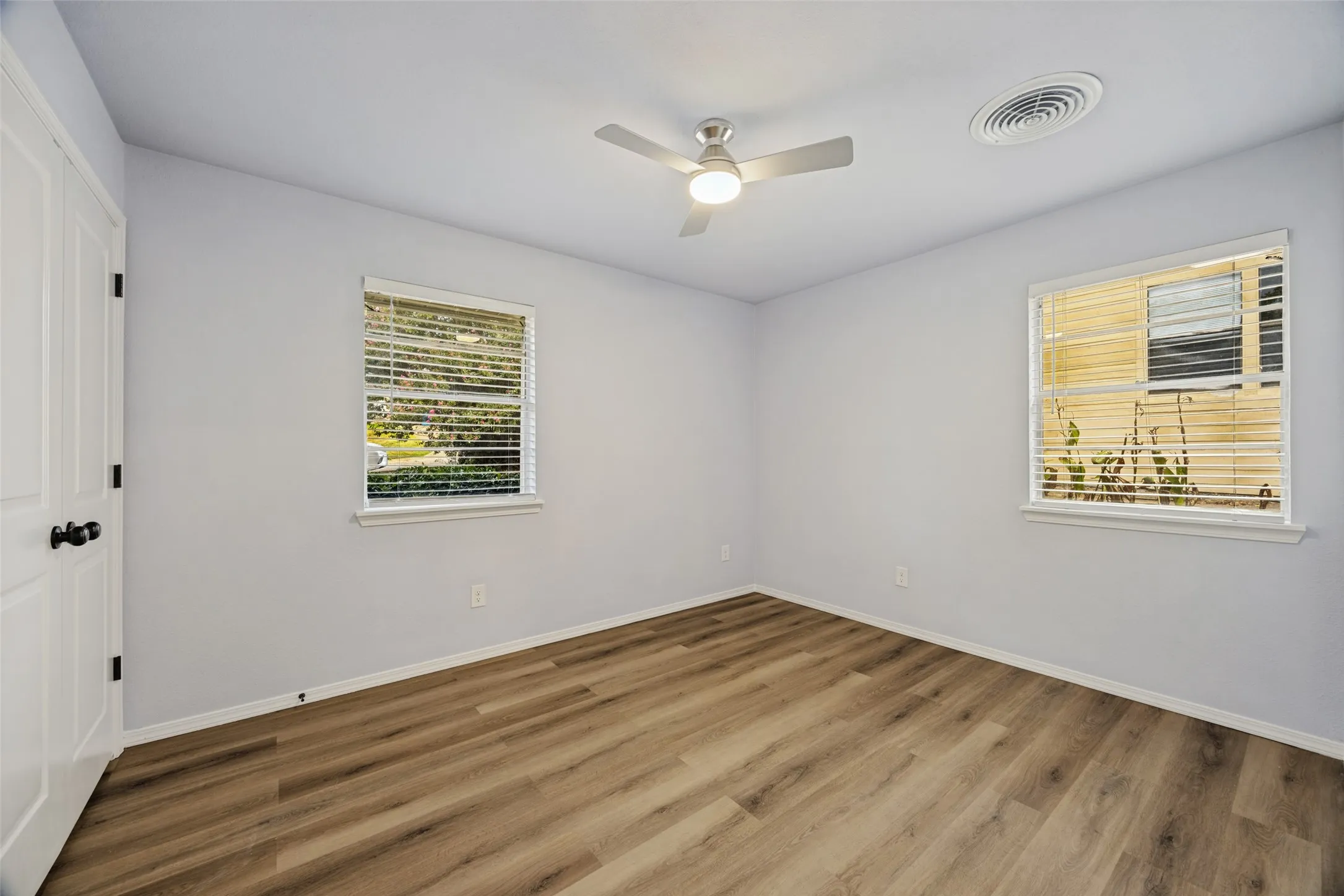 Light-colored walls, wood-finish flooring, and multiple windows with blinds