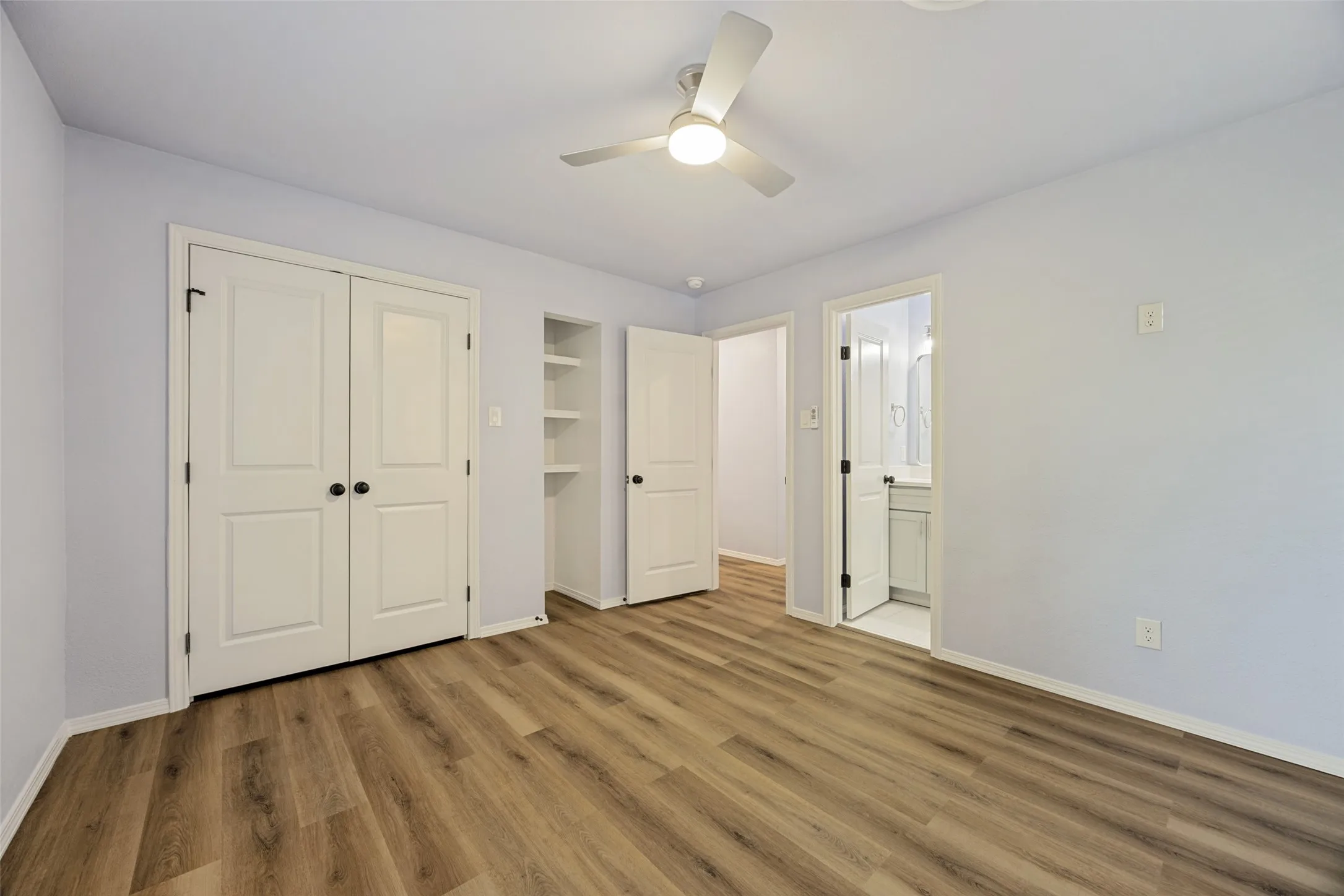 Wood-finish flooring throughout, ceiling fan with integrated lighting, built-in shelving, white paneled doors, and white trim