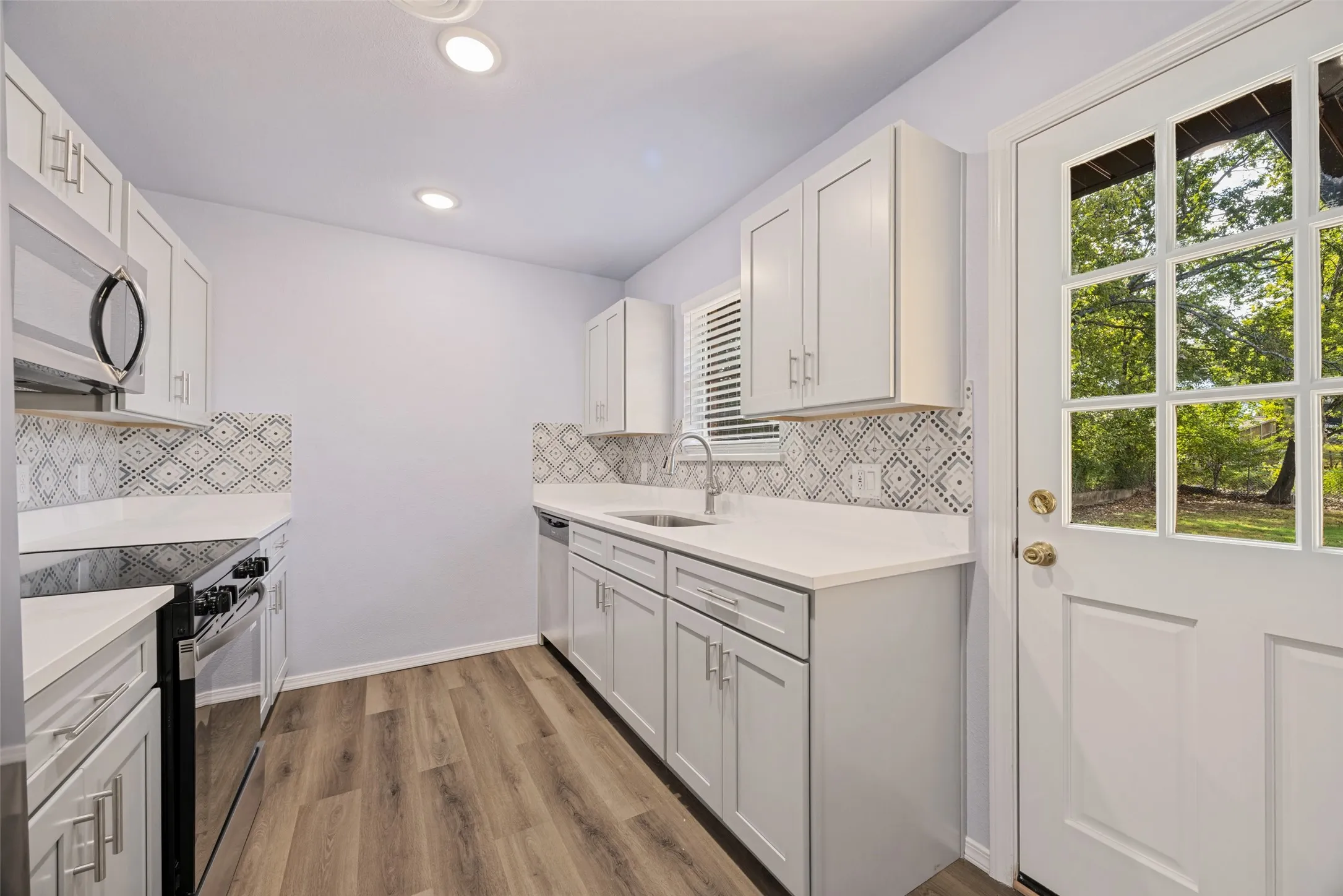 Kitchen featuring shaker-style cabinetry, quartz countertops, patterned tile backsplash, and wood-finish flooring