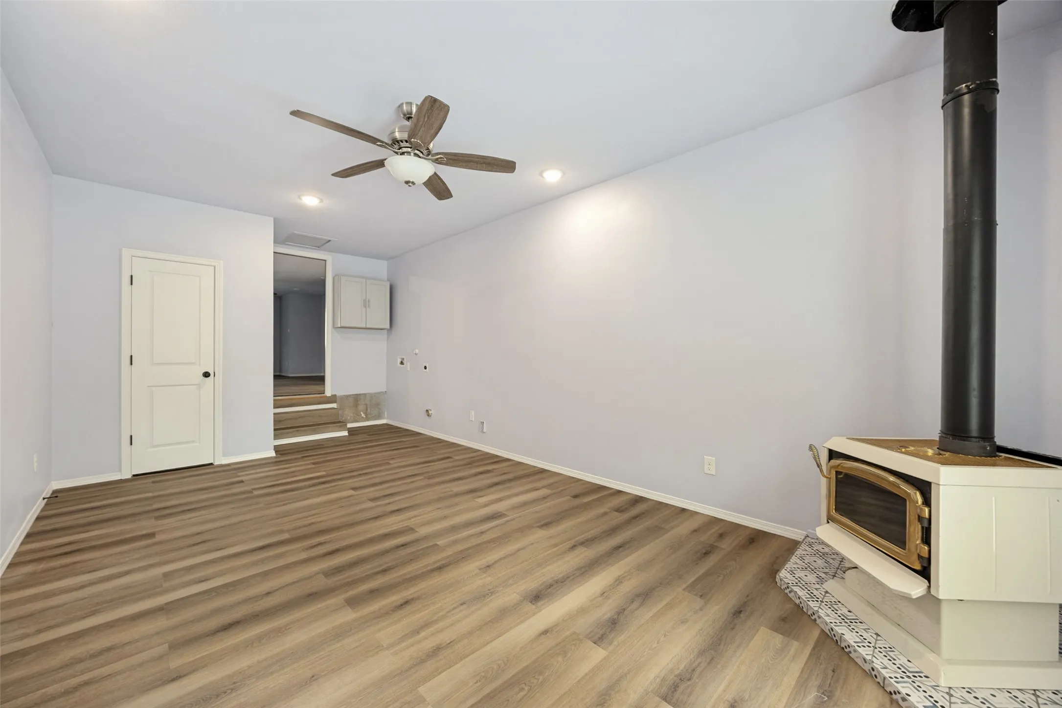 Wood-finish flooring, recessed lighting, ceiling fan, and a freestanding stove with a decorative hearth
