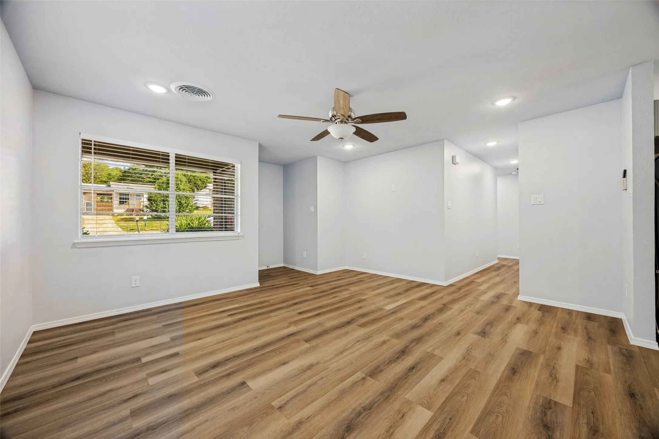 Expansive open-concept room featuring wood-finish flooring, a ceiling fan, recessed lighting, and a large window with blinds