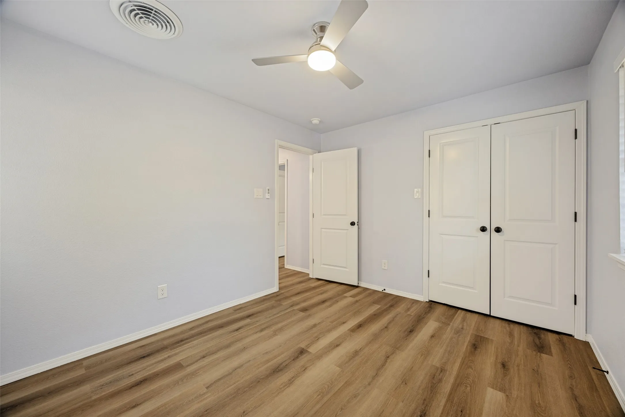 Wood-finish flooring, white paneled doors with matte black hardware, and a ceiling fan with integrated lighting
