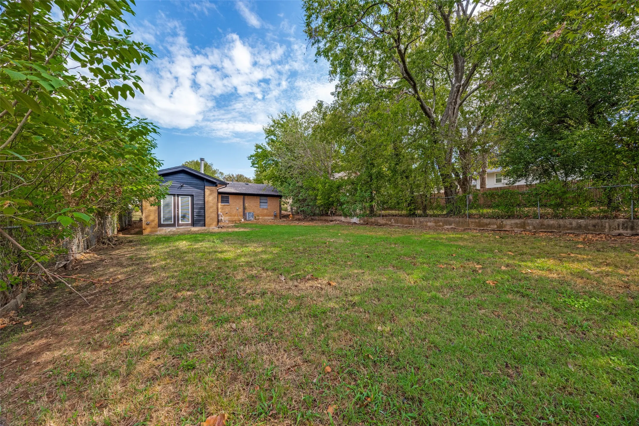 Expansive backyard featuring mature trees and a chain-link fence