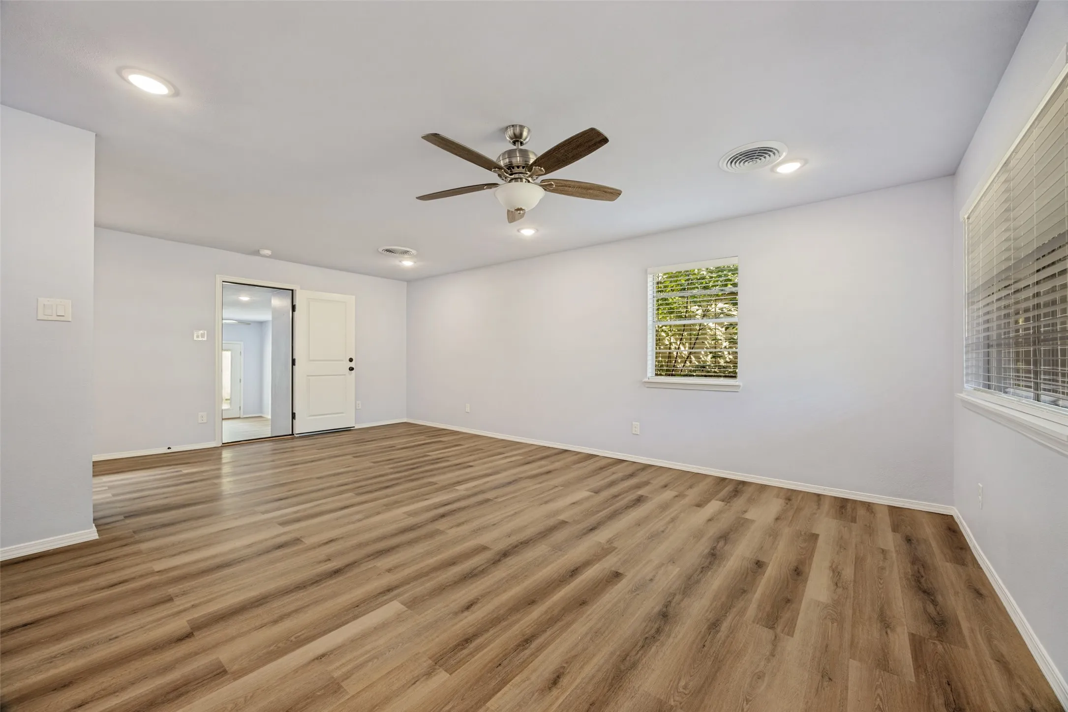 Spacious room featuring wood-finish flooring, recessed lighting, a ceiling fan, and multiple windows