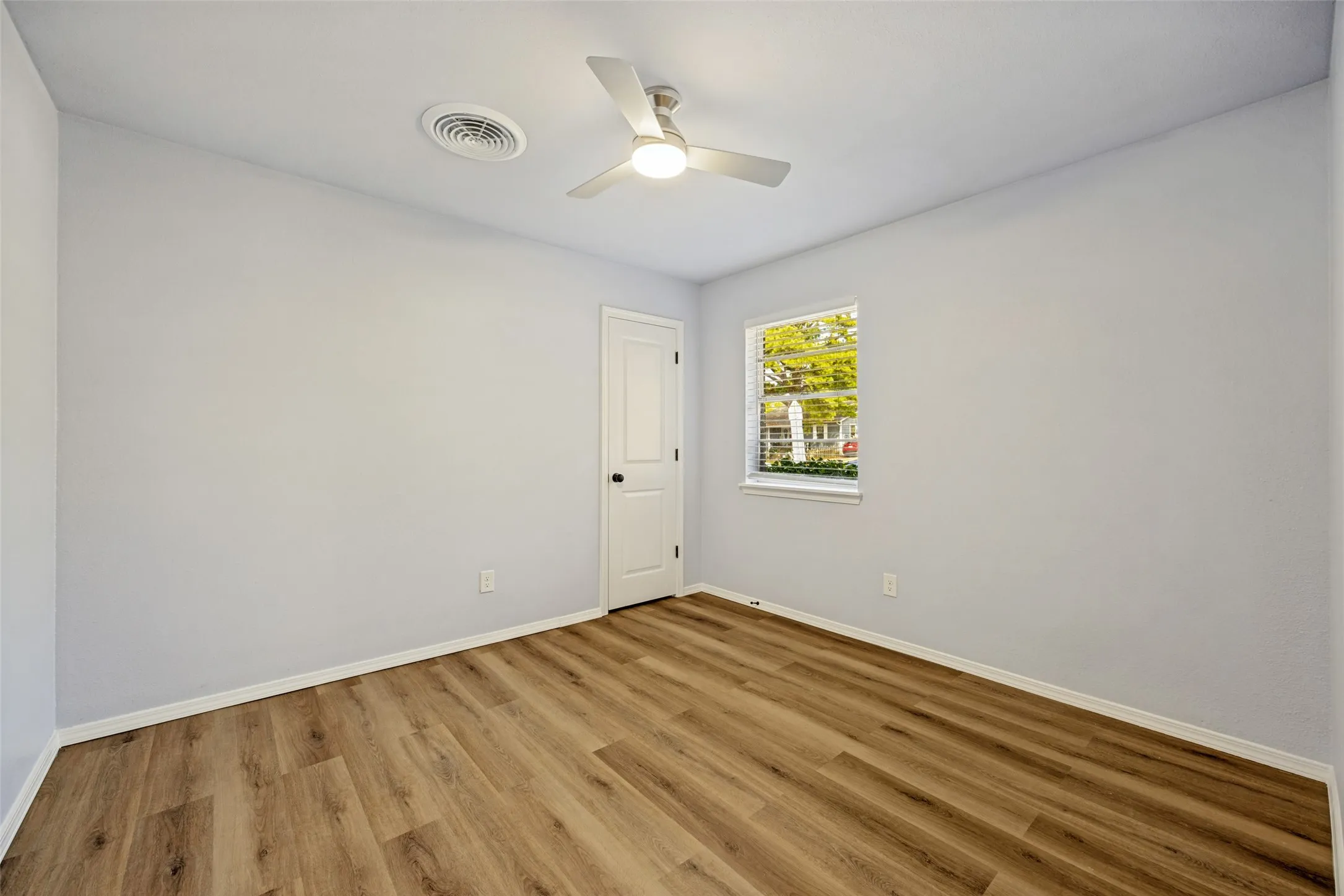 Wood-finish flooring, white walls, ceiling-mounted fan with integrated lighting, white interior door, and window with white blinds