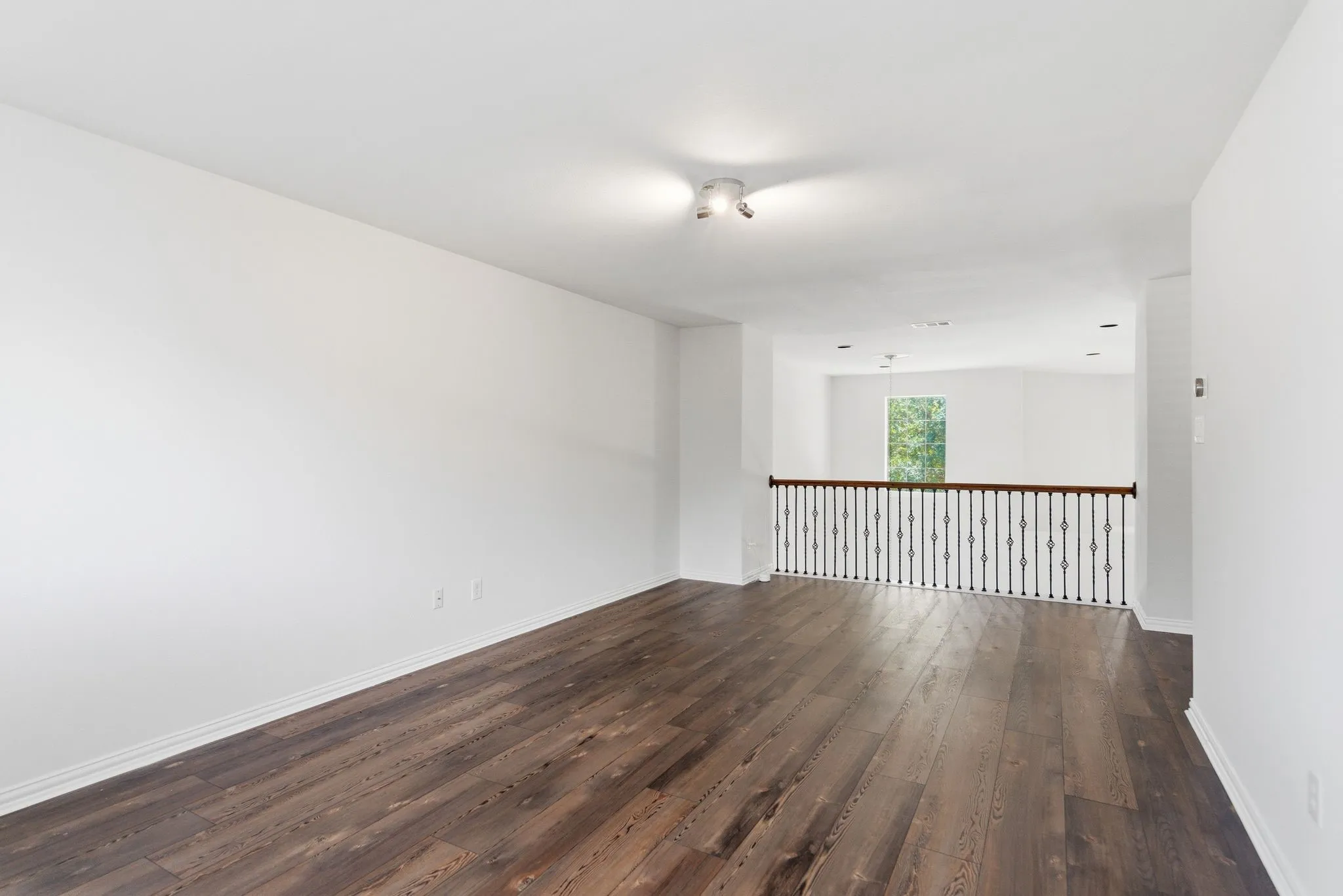 Spacious room featuring wood-finish flooring, crisp white walls, and a track lighting fixture