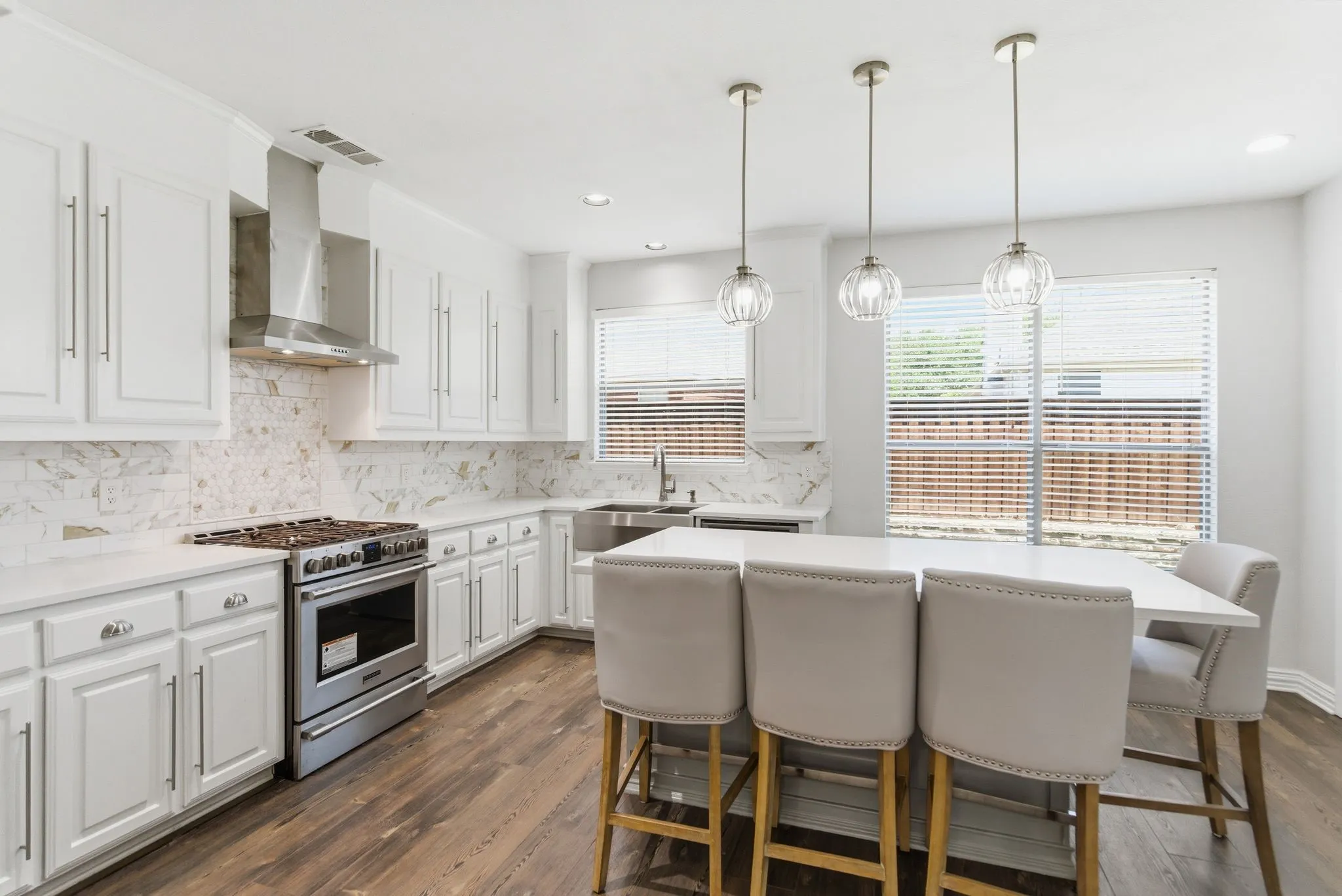 White cabinetry, stainless steel appliances, wood-finish flooring, island with pendant lighting, and a tile backsplash