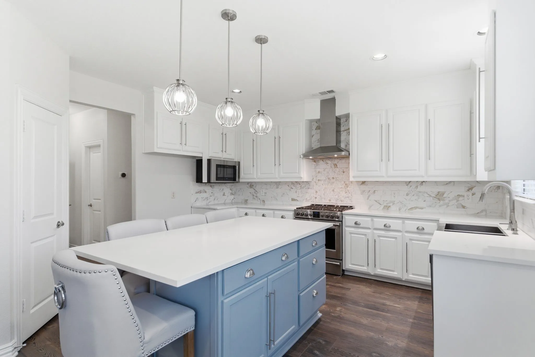 Kitchen featuring white cabinetry, a light blue island with a white countertop, wood-finish flooring, a stainless steel range with a coordinating hood, and a patterned tile backsplash