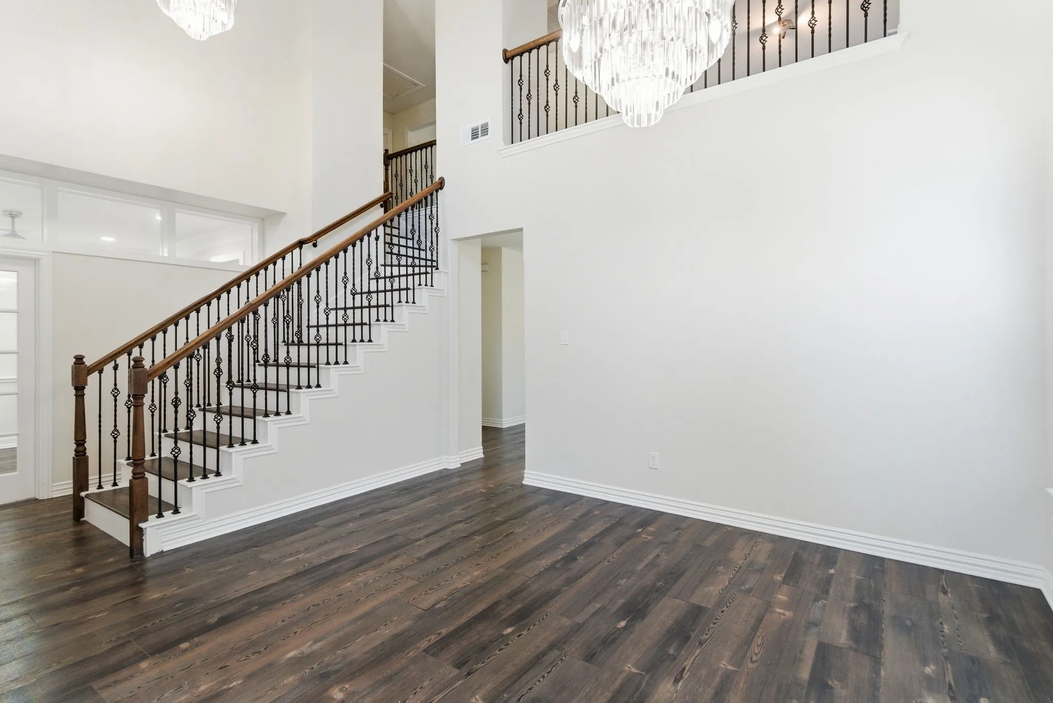 Double-height foyer featuring a grand staircase with dark wood banisters and wrought-iron balusters, wood-finish flooring, and a multi-tiered chandelier