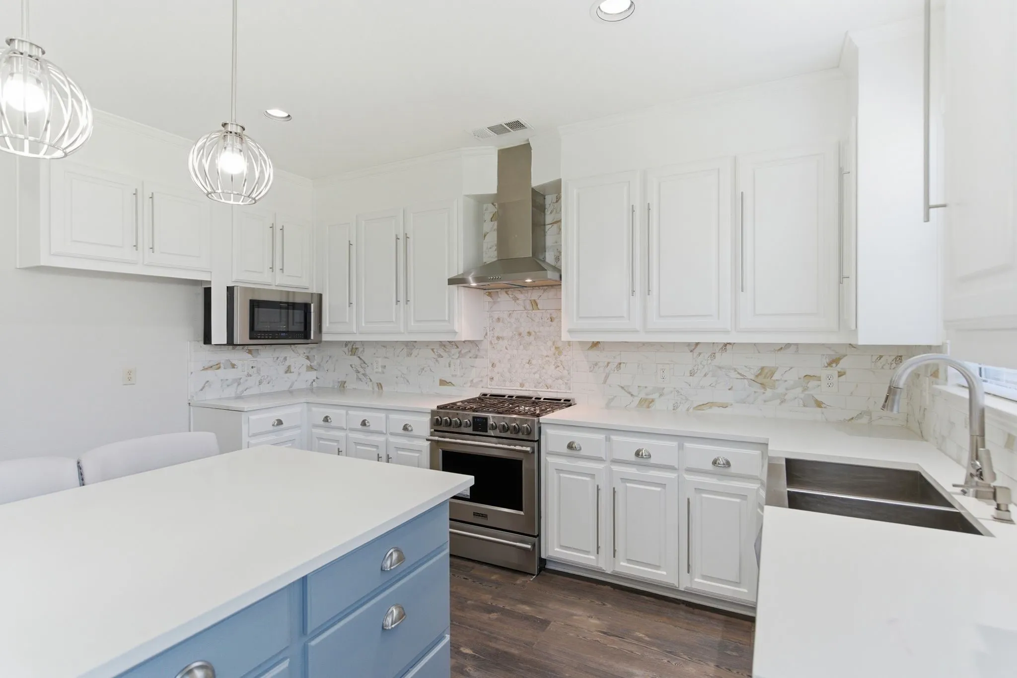 White cabinetry with brushed nickel hardware, stainless steel appliances, a center island with contrasting blue base, white countertops, and a white and gold-toned backsplash