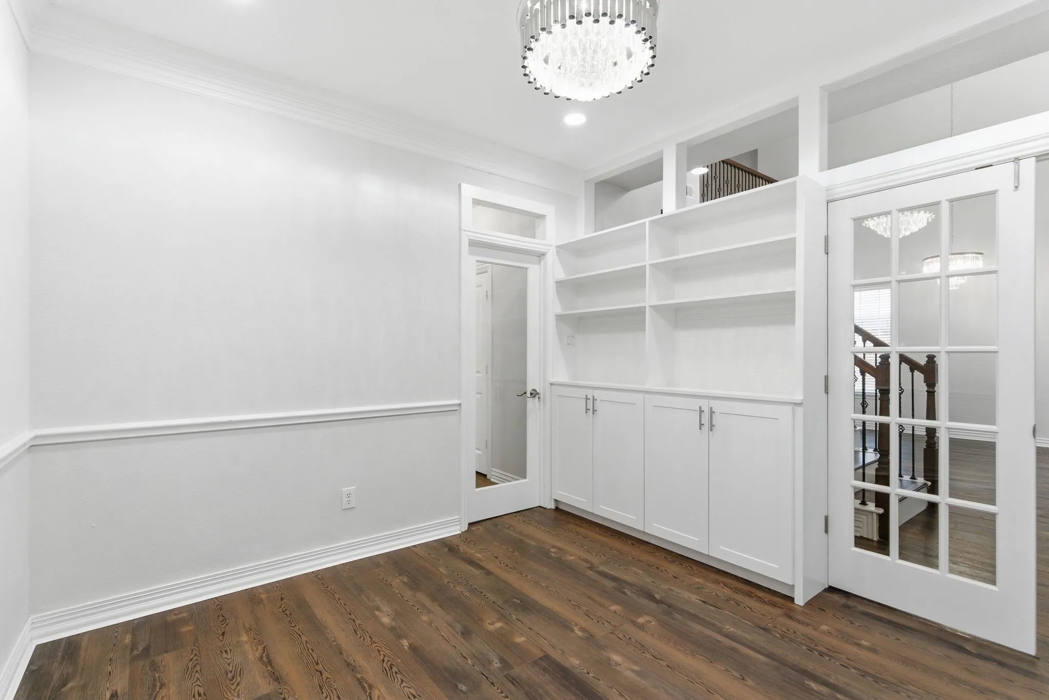 Wood-finish flooring, built-in shelving, white cabinetry, French doors with glass panes, and a decorative ceiling fixture
