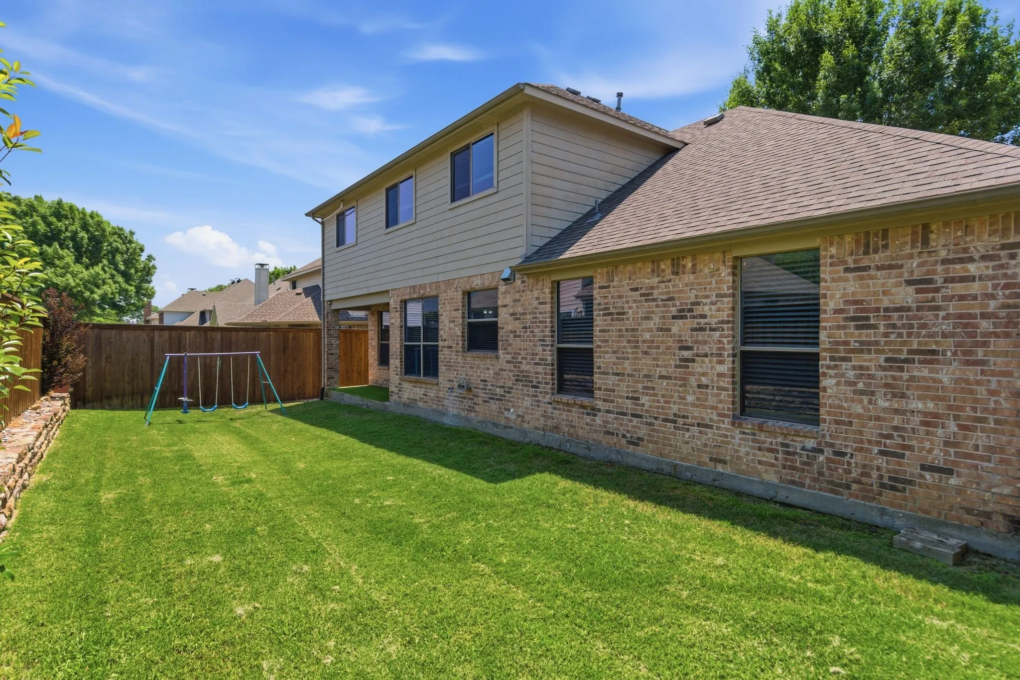 Brick and siding exterior, shingle roof, green lawn, wood fence, retaining wall