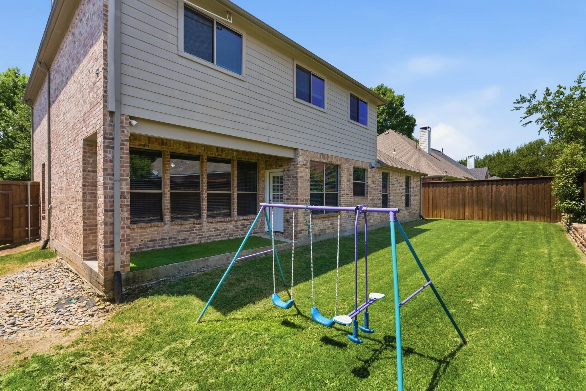 Expansive grassy backyard featuring a full privacy fence and a brick-clad retaining wall