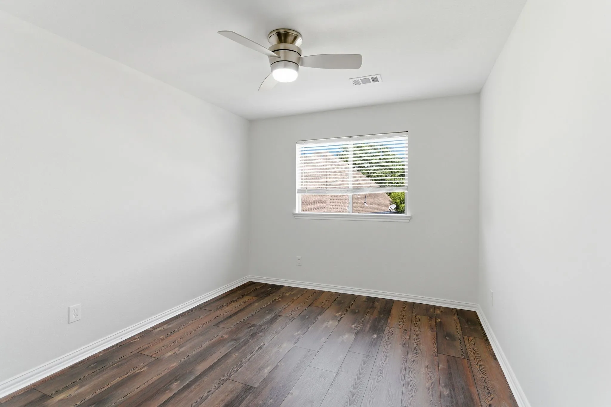 Rich wood-finish flooring, a contemporary ceiling fan with integrated lighting, and a single window with horizontal blinds