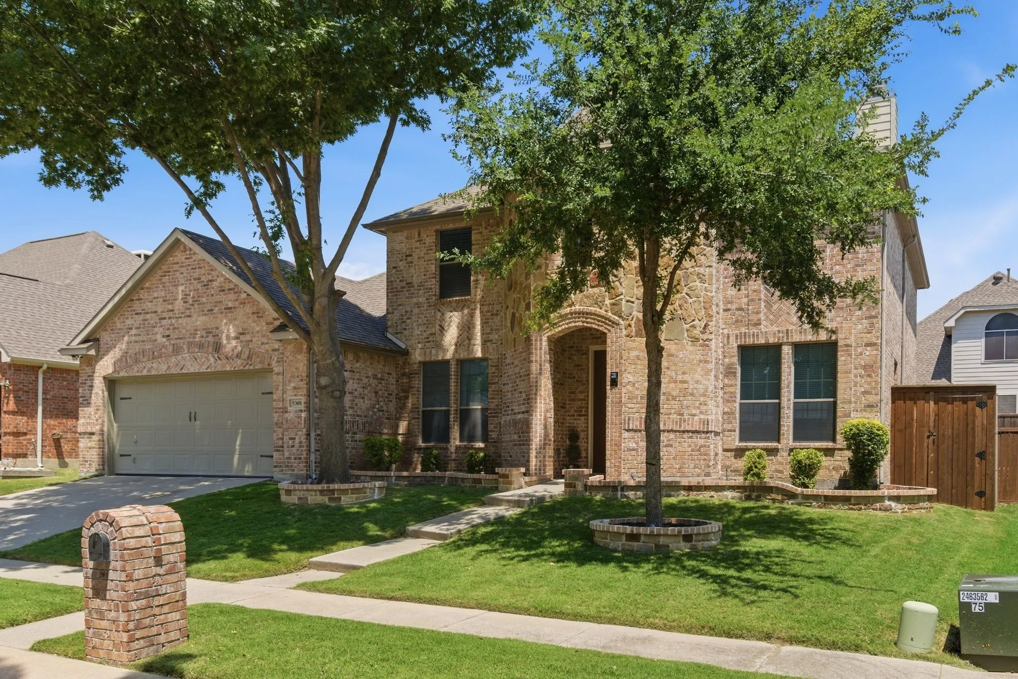 Brick exterior, arched entry, attached two-car garage, mature landscaping, and a brick mailbox
