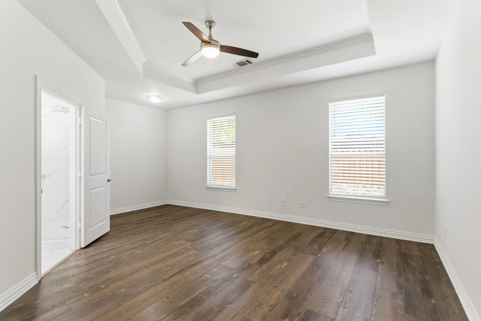 Tray ceiling with crown molding, wood-finish flooring, two windows with blinds, recessed lighting, and a ceiling fan
