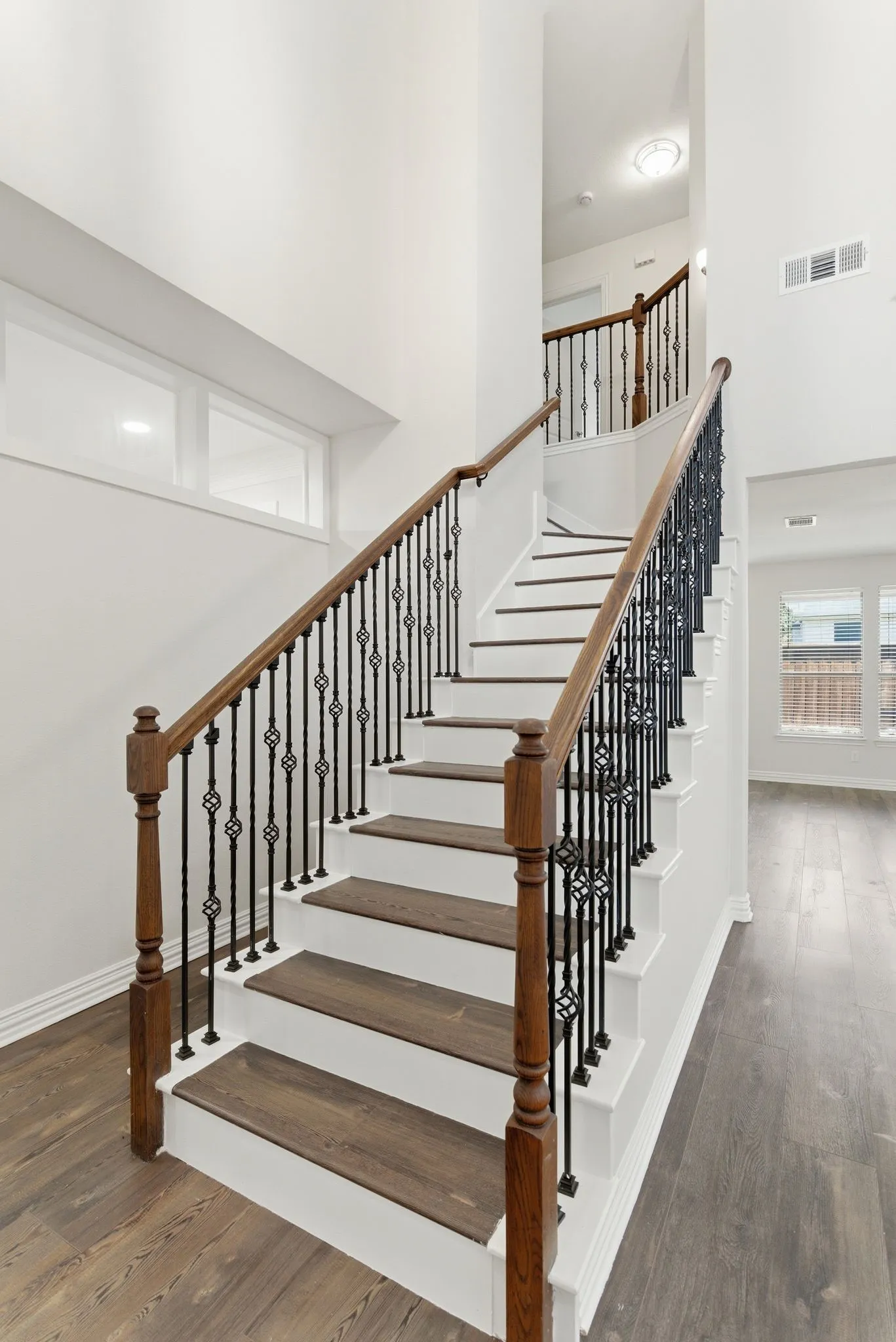 Staircase featuring wood-finish treads and risers, wrought iron balusters, and a rich wood handrail