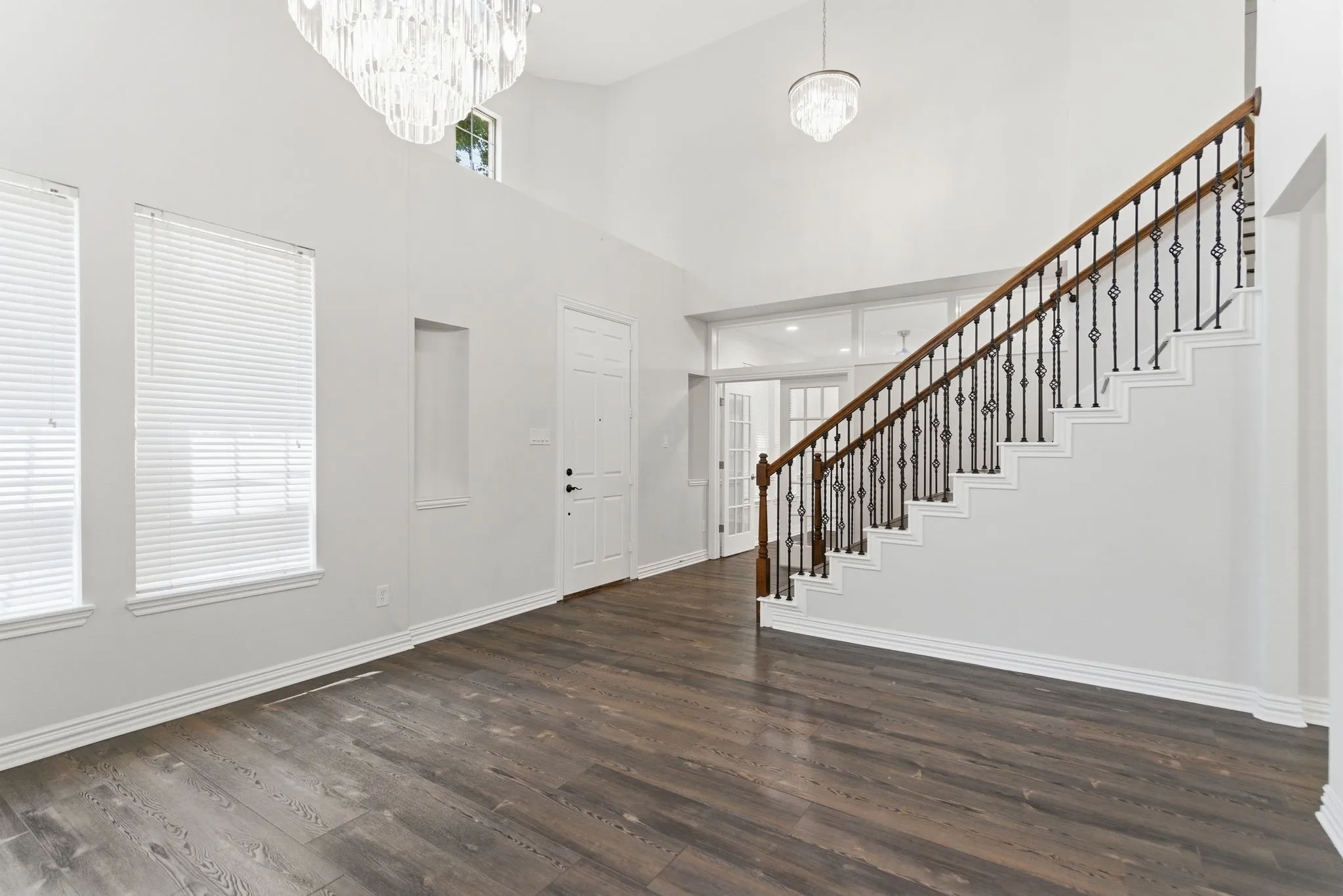 Vaulted entryway featuring wood-finish flooring, a grand staircase with wrought iron balusters, and a tiered chandelier
