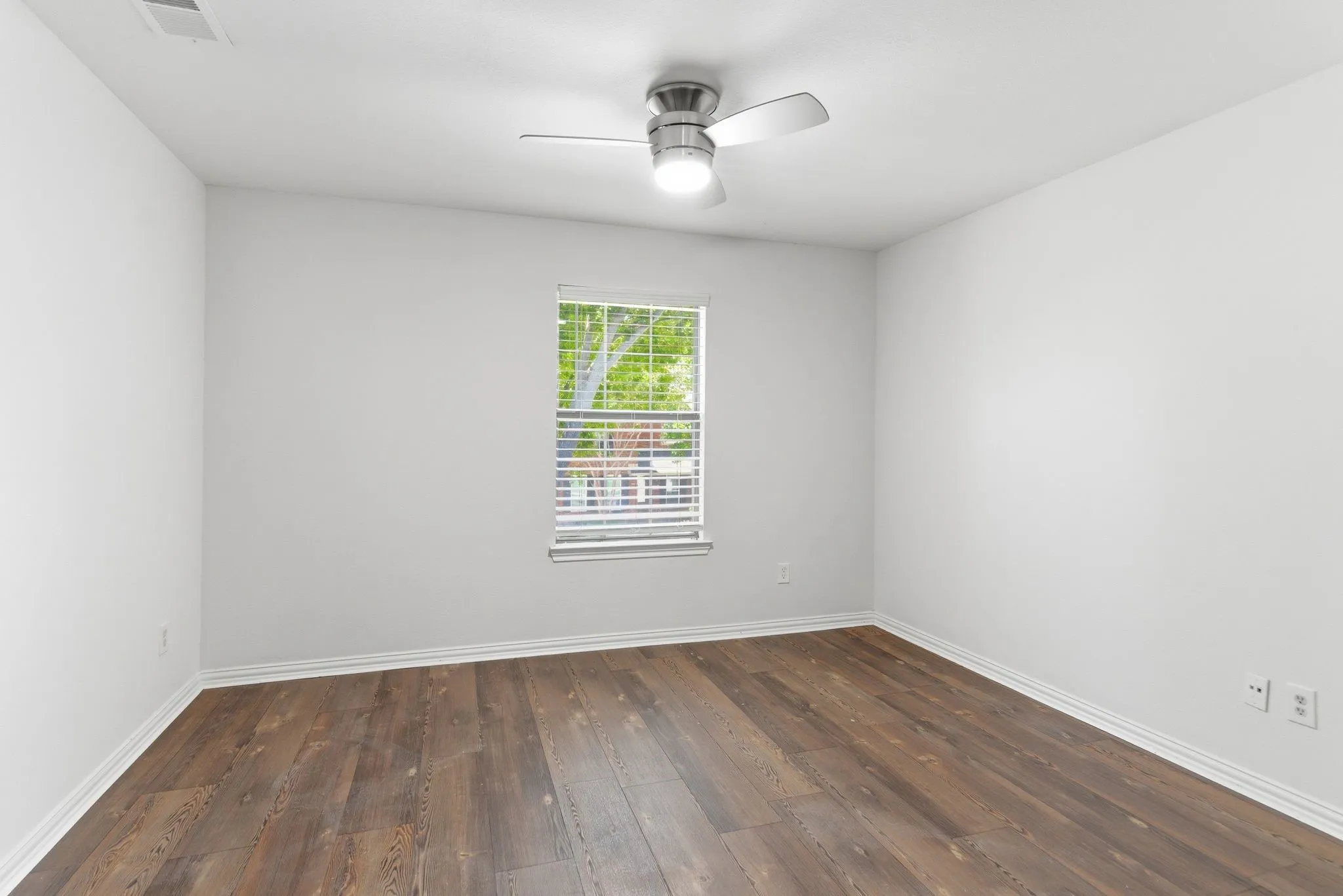 Wood-finish flooring, white walls, window with blinds, and a ceiling fan with integrated lighting