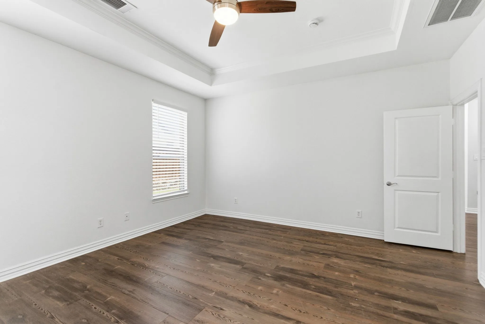Wood-finish flooring, tray ceiling, ceiling fan, and window with blinds
